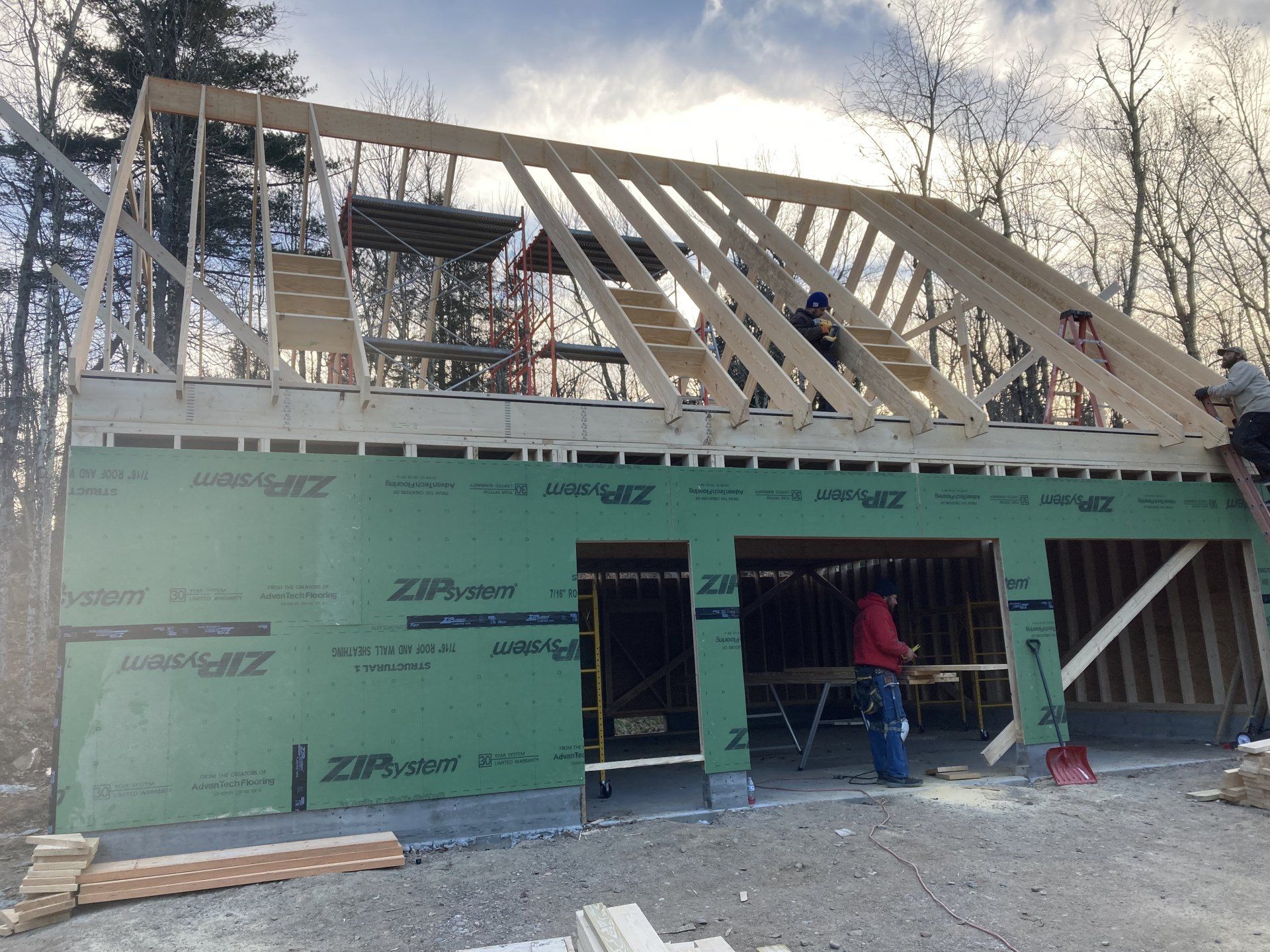 Partially built house with green siding, exposed roof framing, and a worker near the front entrance