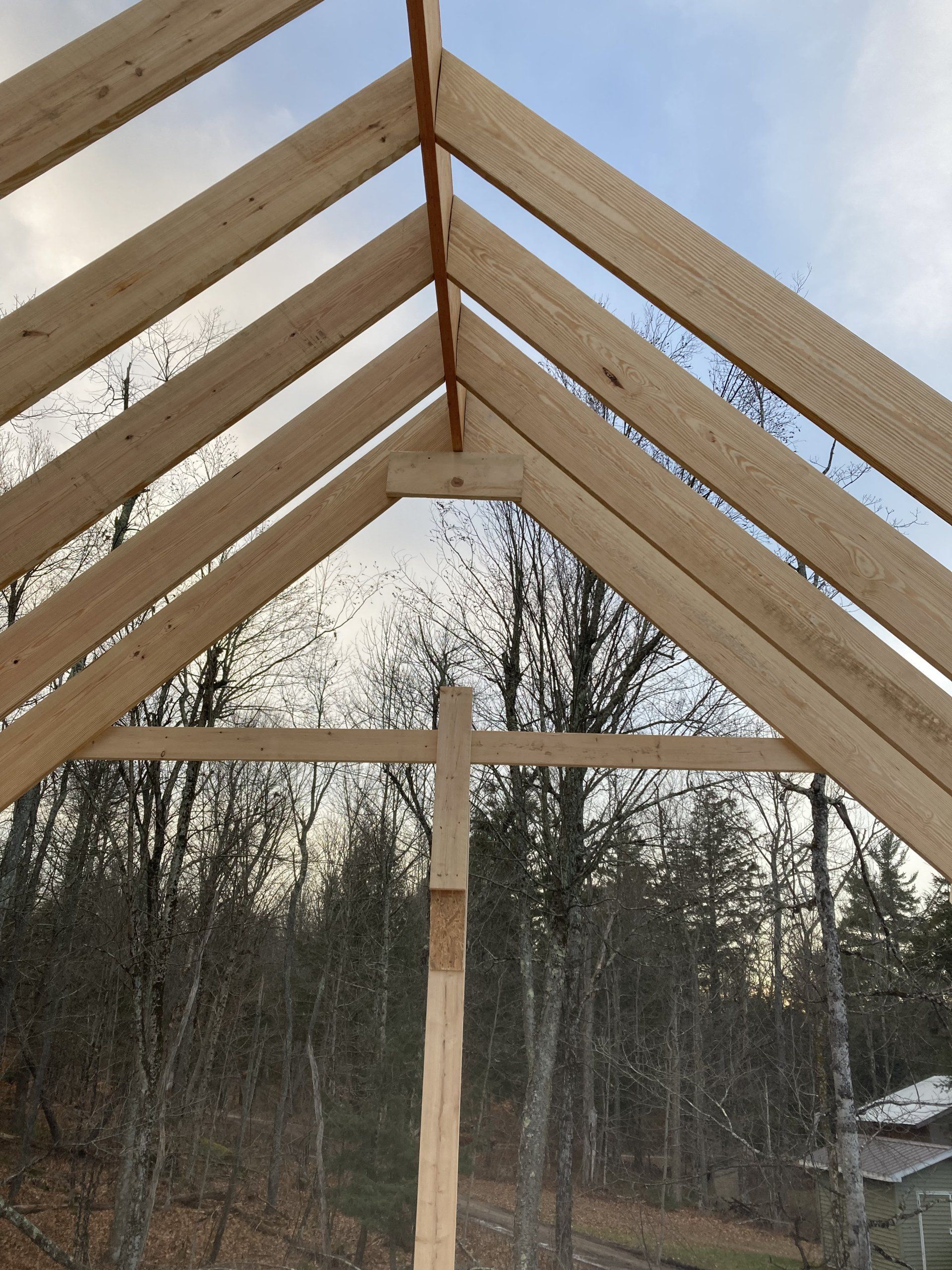 Wooden roof frame under construction against a cloudy sky, with trees in the background