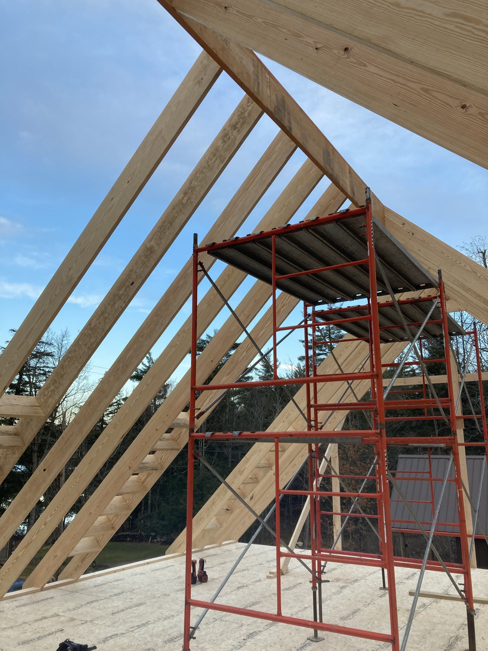 Red scaffolding under a slanted wooden roof frame at a construction site