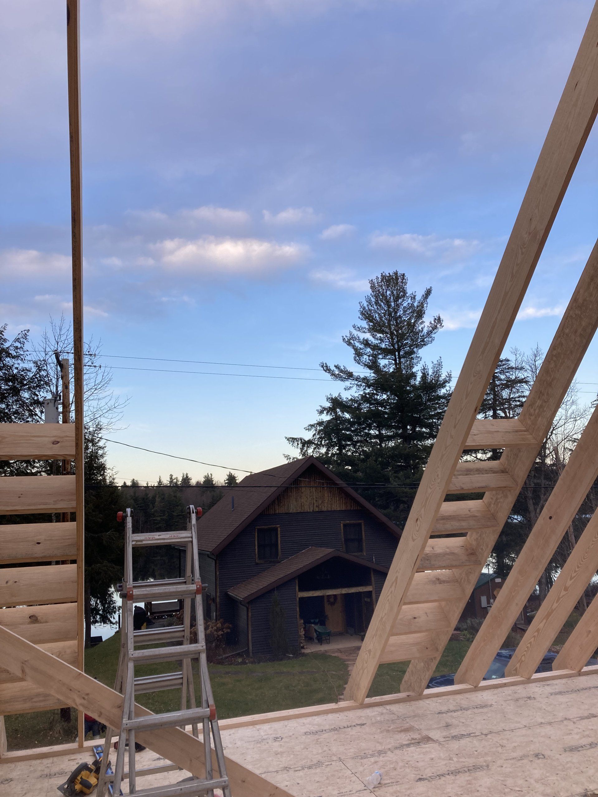 Wooden deck framing with ladder, overlooking a cabin and lake at dusk