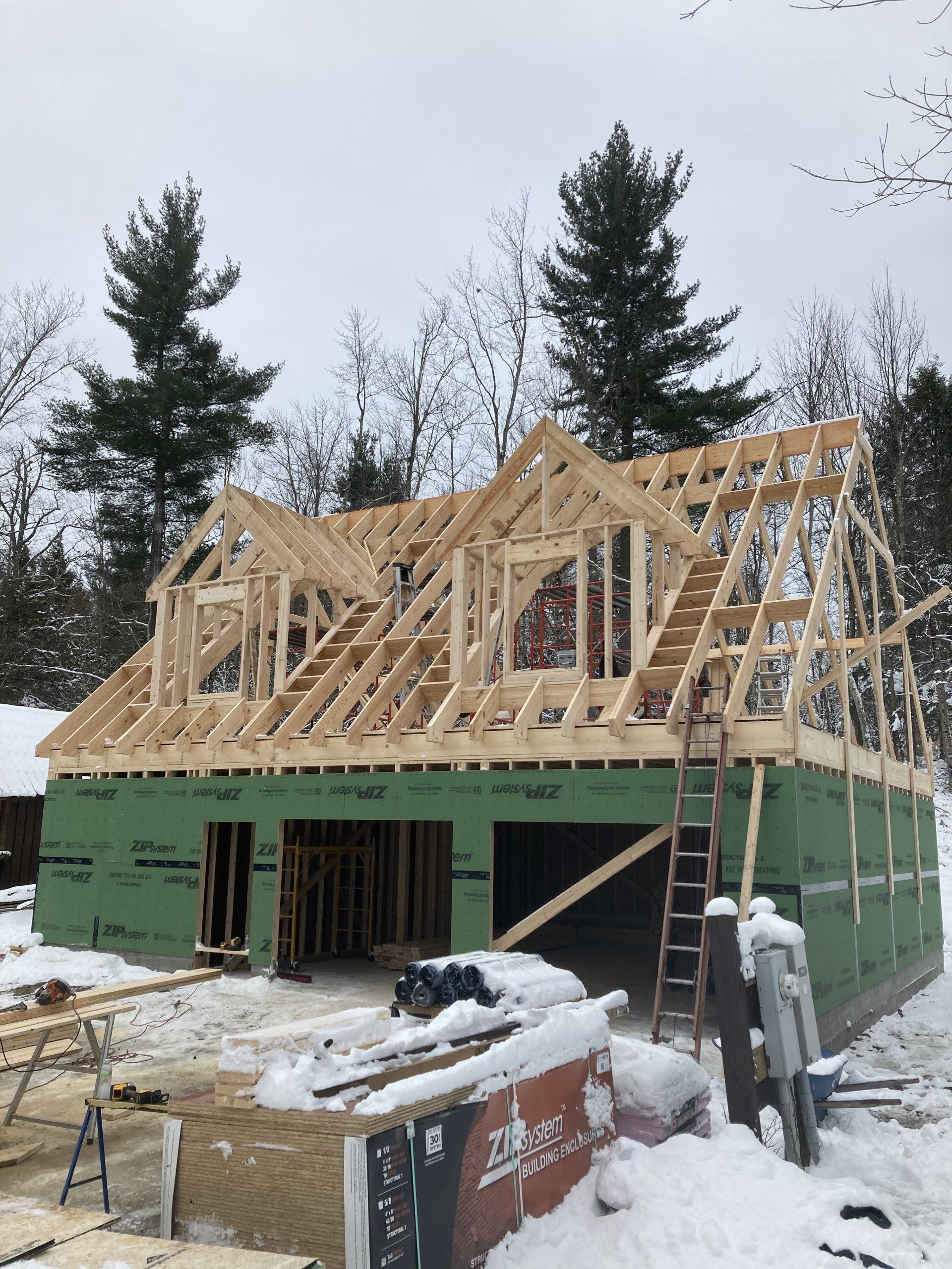 Snowy house under construction with green walls and exposed wooden roof framing