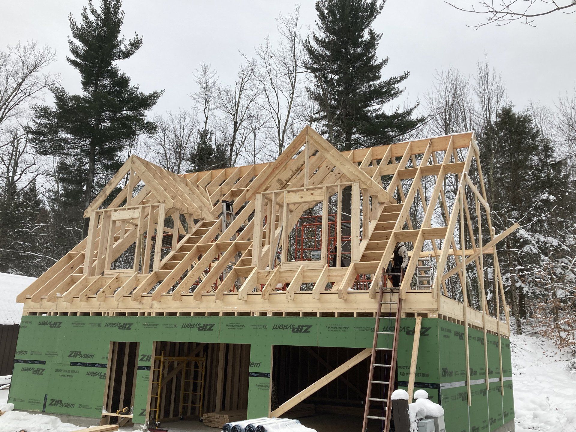 Partially built house with wooden roof framing and green sheathing in a snowy wooded area
