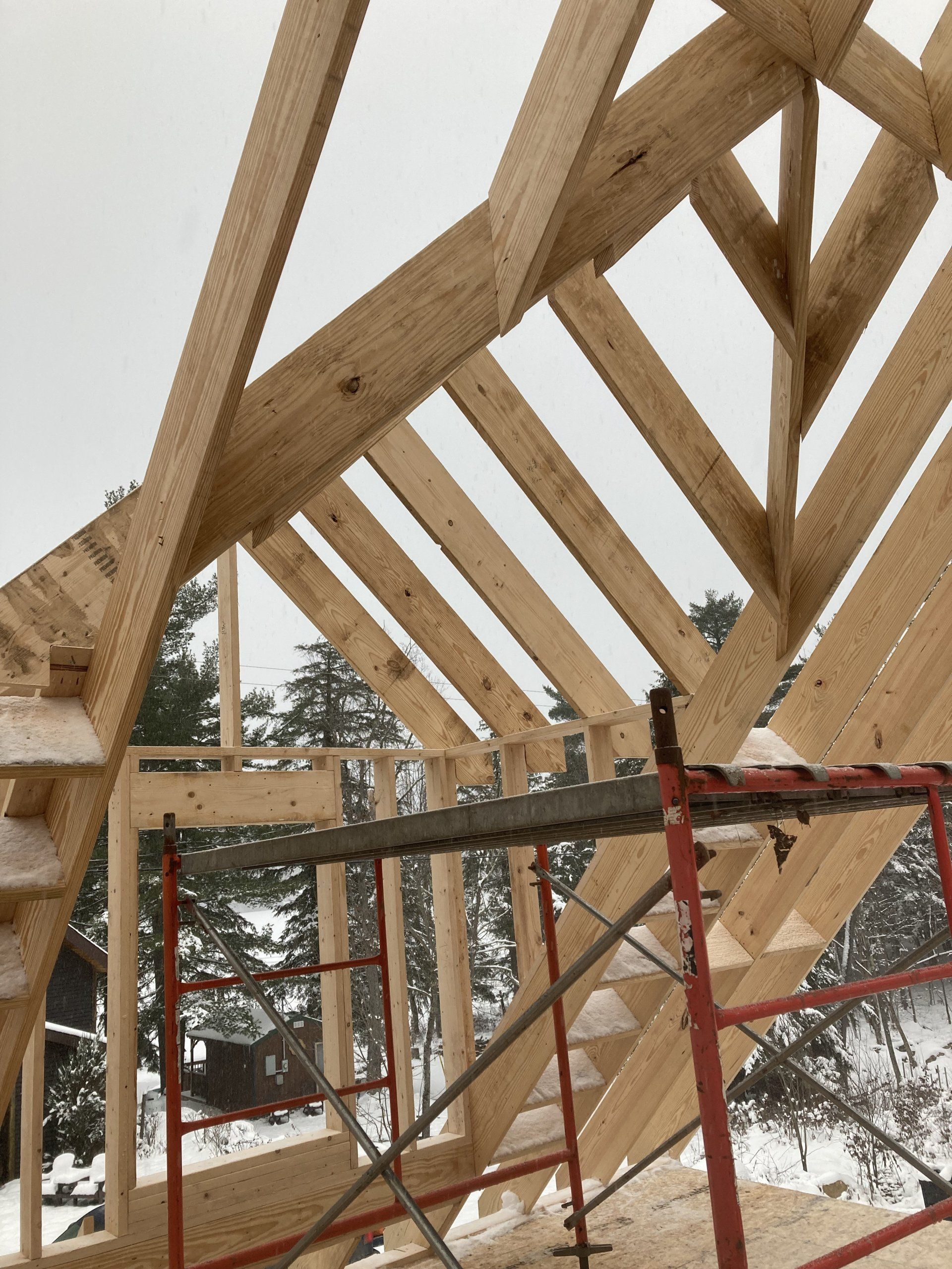 Wooden roof trusses under construction with red scaffolding in a snowy outdoor setting