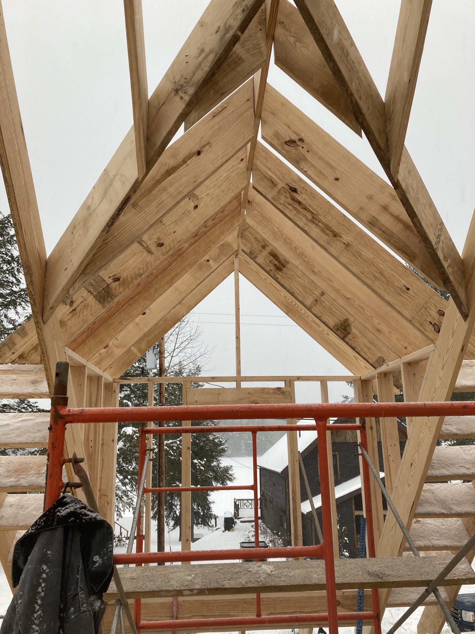 Wooden roof framing under construction with orange scaffolding in a snowy outdoor setting