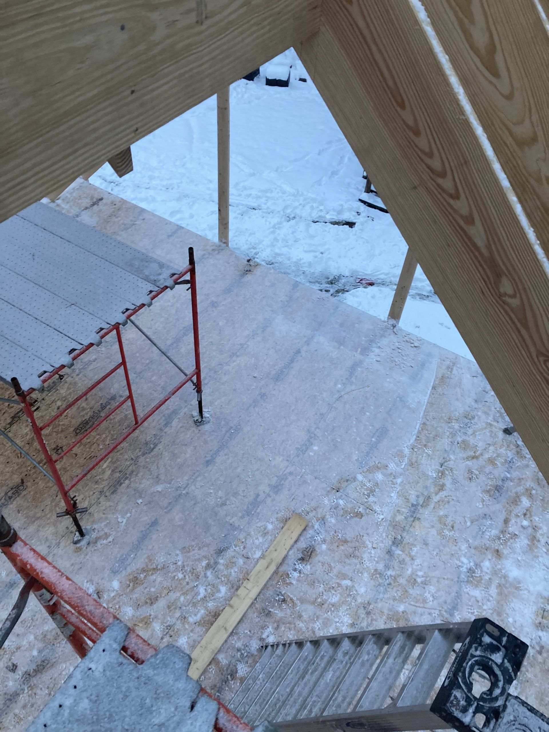 Snow-covered construction stairs with red scaffolding and a wooden frame overhead