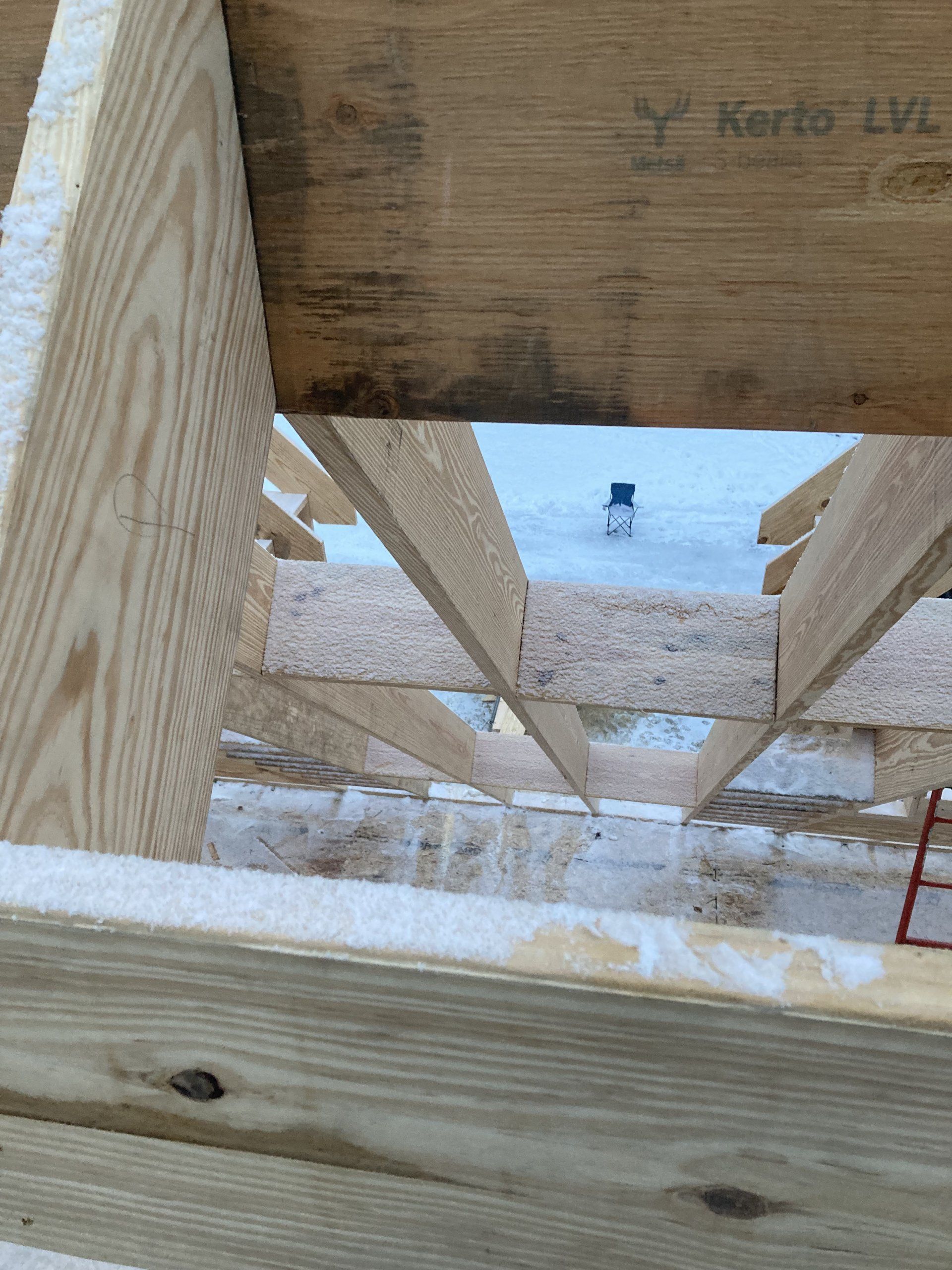 Wooden deck framing with snow-covered ground and a snowy landscape beyond the structure.