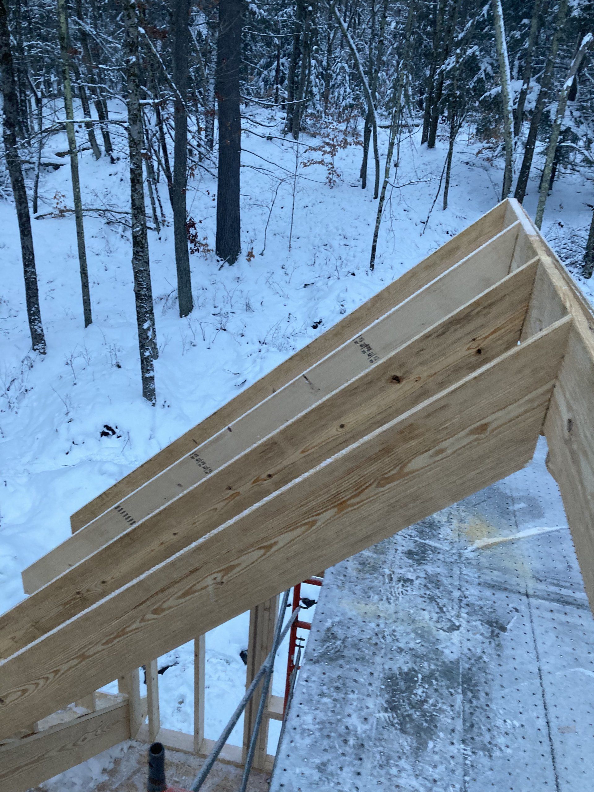 Wooden roof frame under construction beside a snowy forest.