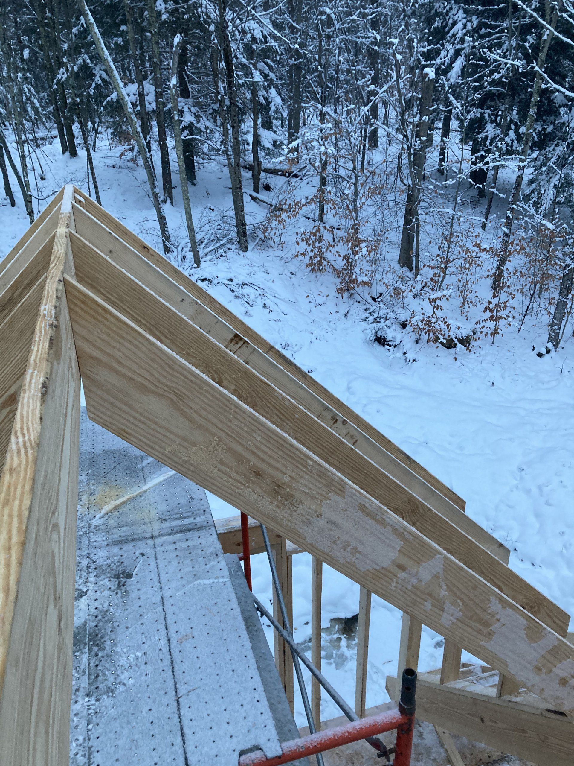 Wooden house roof framing under construction in a snowy wooded area