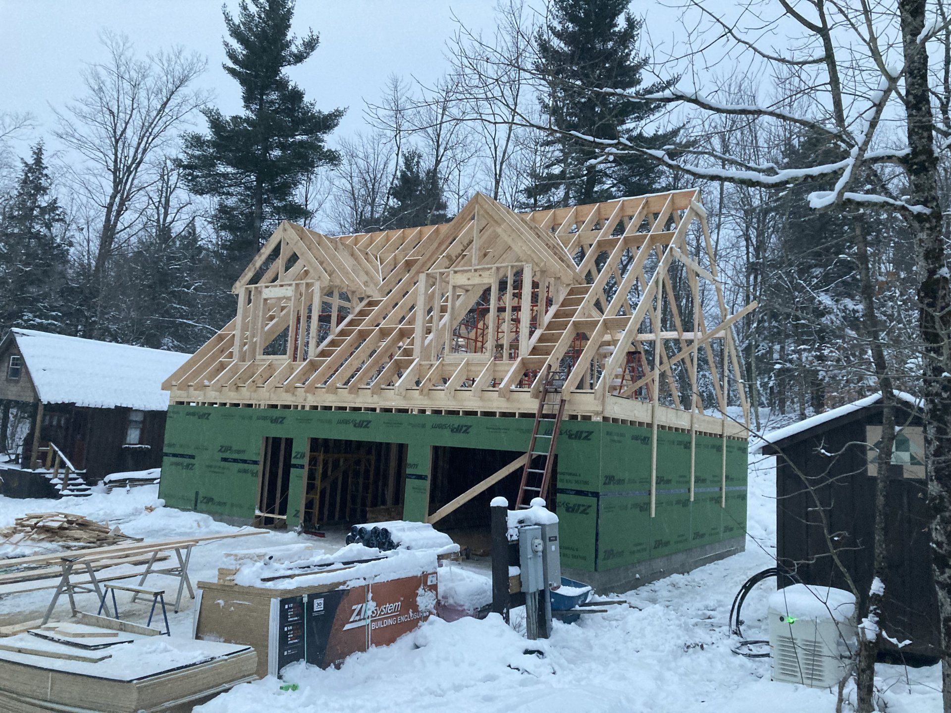 Snowy house under construction with exposed roof framing and green sheathing in a winter yard