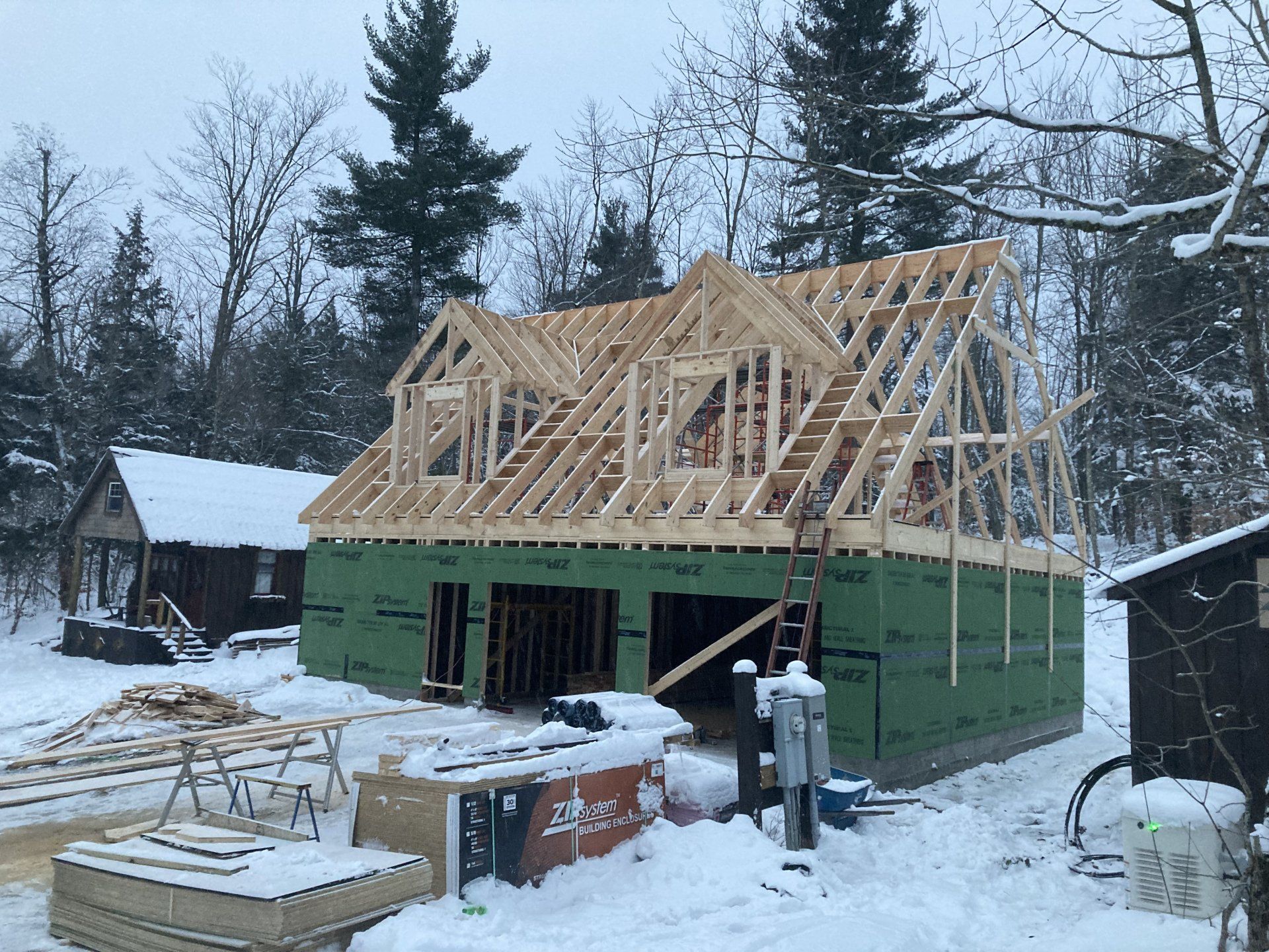 House under construction with exposed wooden roof framing in a snowy yard