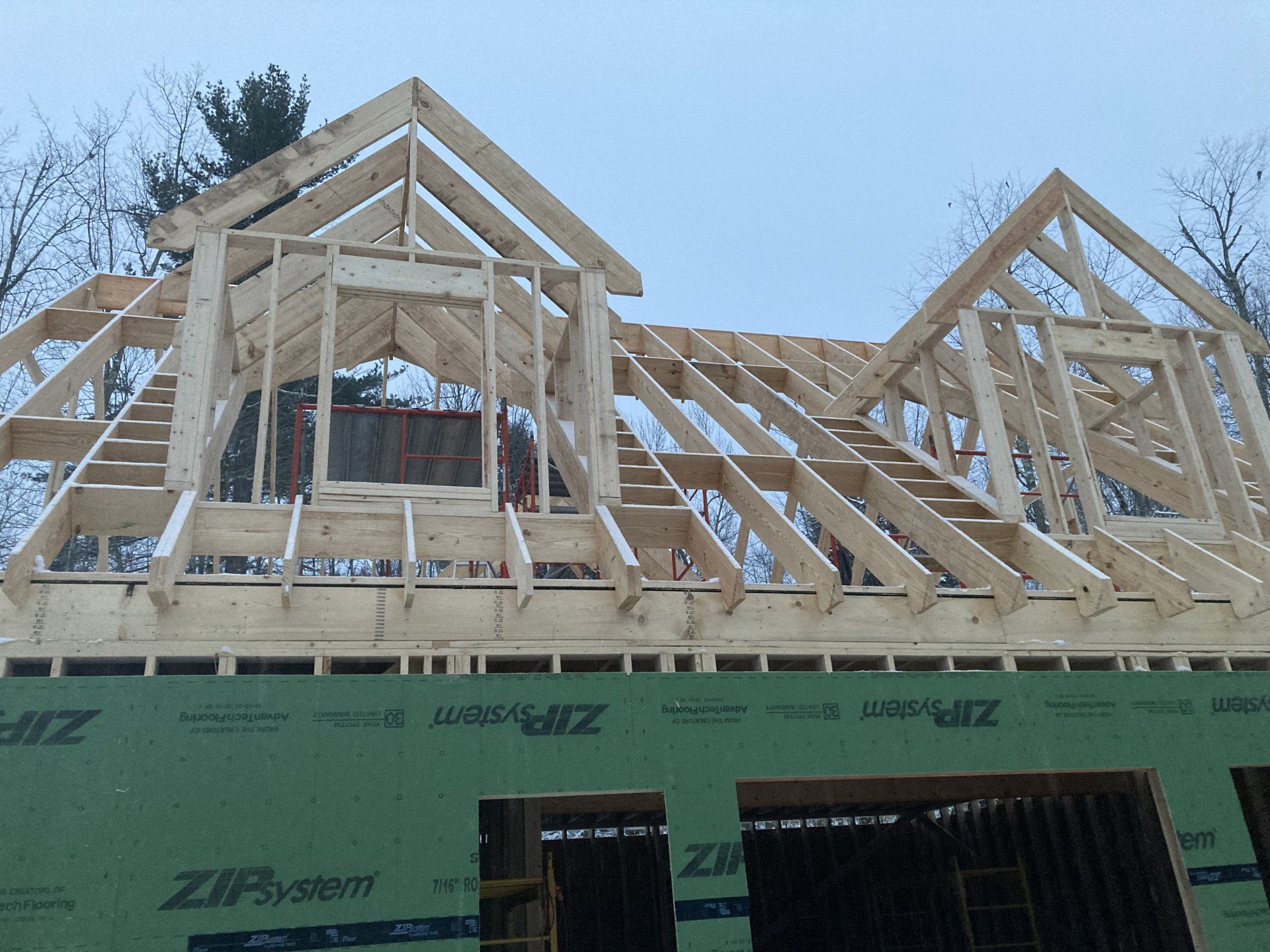 House framing under construction with exposed wooden roof trusses and green sheathing.