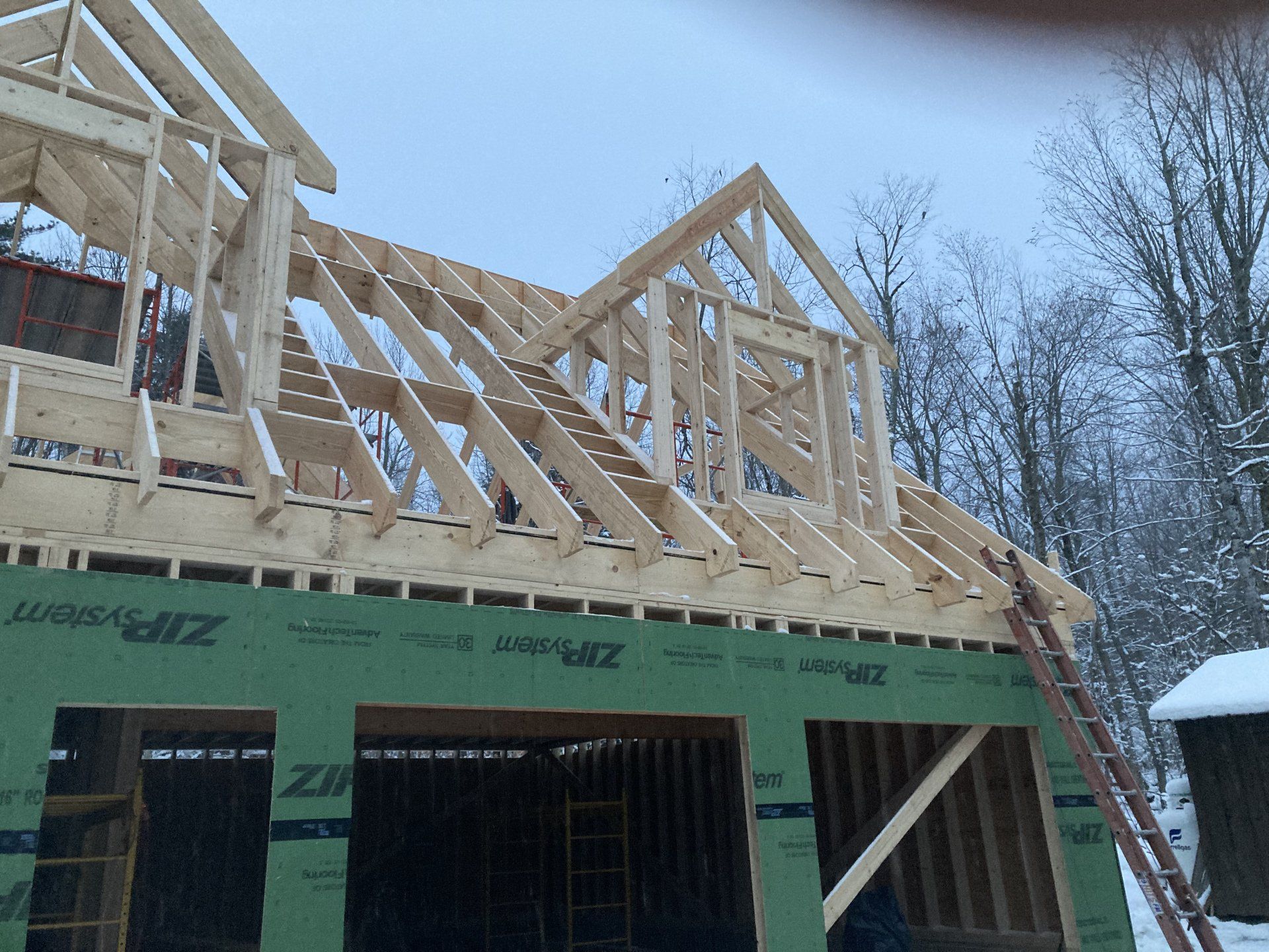 Partially framed house under construction with green sheathing and a snowy winter background