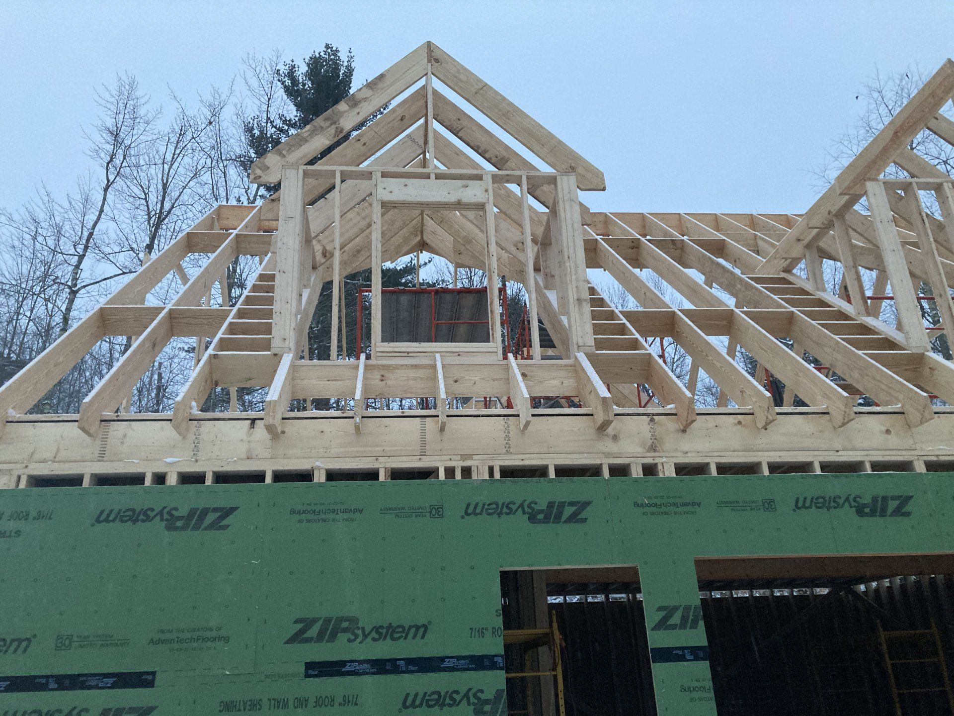 Wooden house roof framing under construction with green ZIP sheathing and exposed trusses
