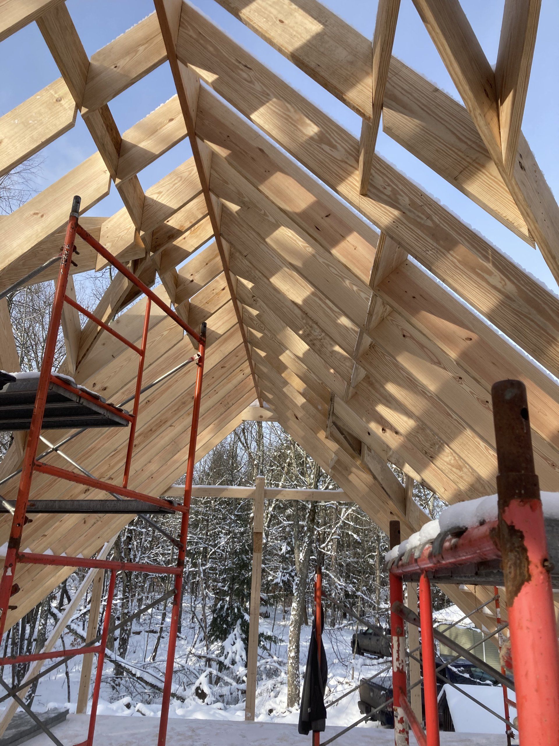 Wooden roof frame under construction with red scaffolding and snow visible outside.