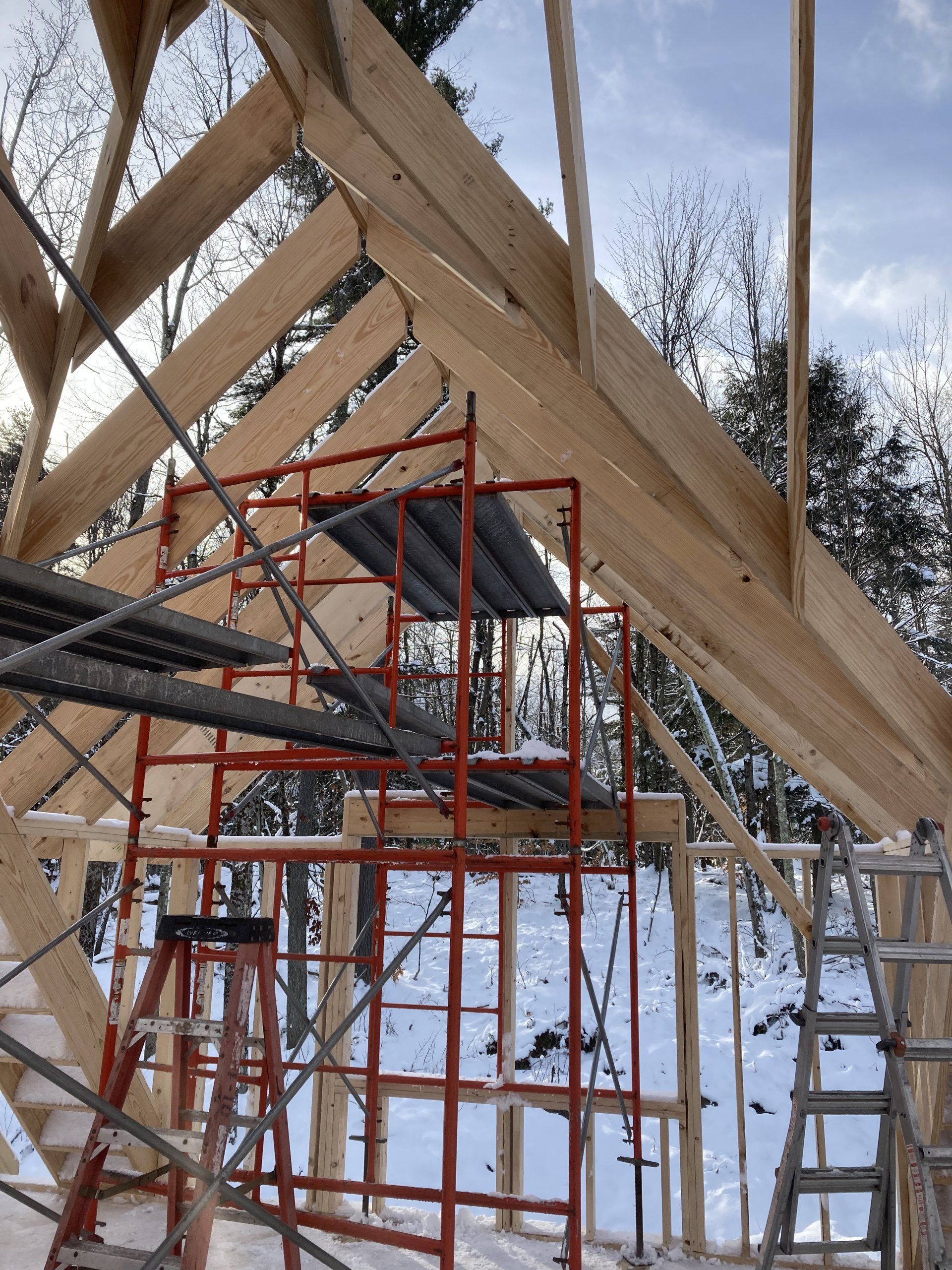 Scaffolding beneath a timber roof frame at a snowy construction site