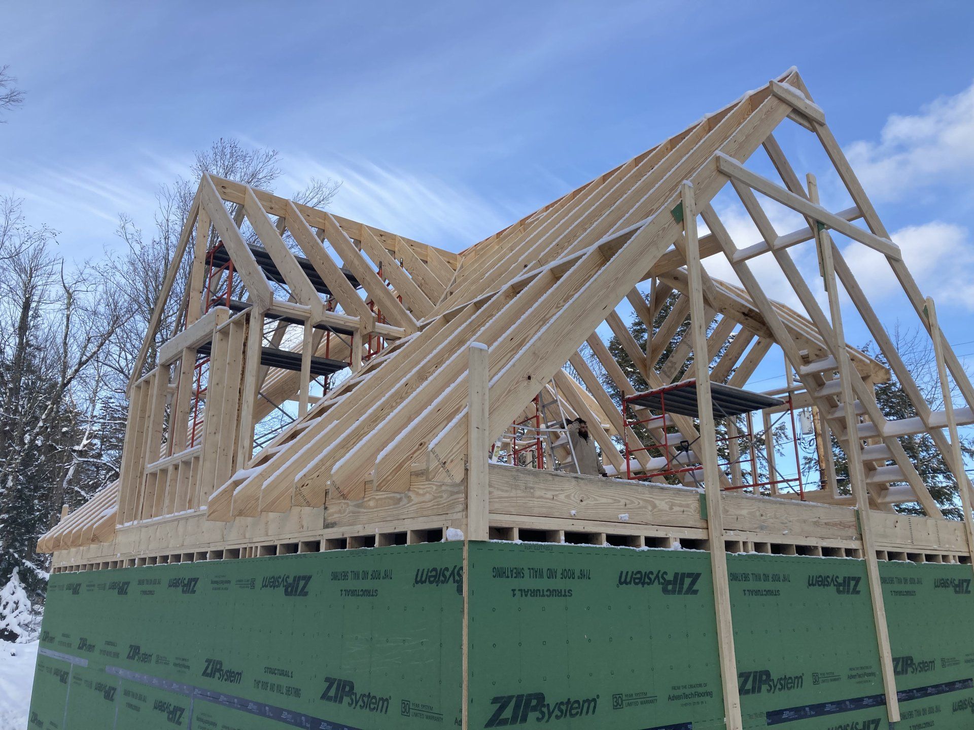 Wood-framed house under construction with green sheathing and snow on the ground