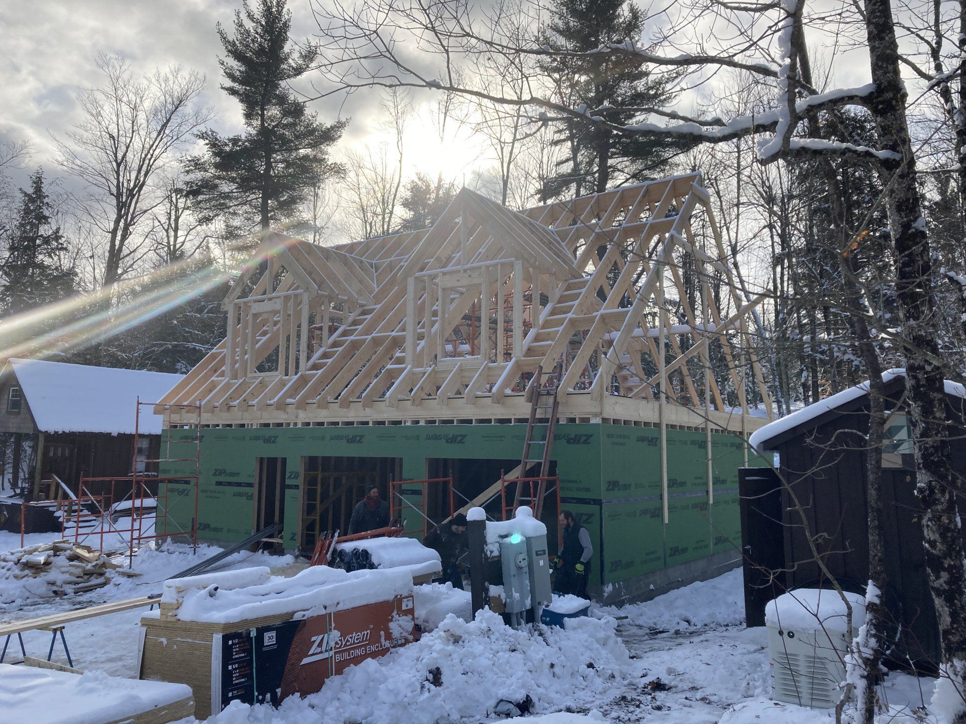 Partially built house with exposed roof framing in a snowy yard at sunset