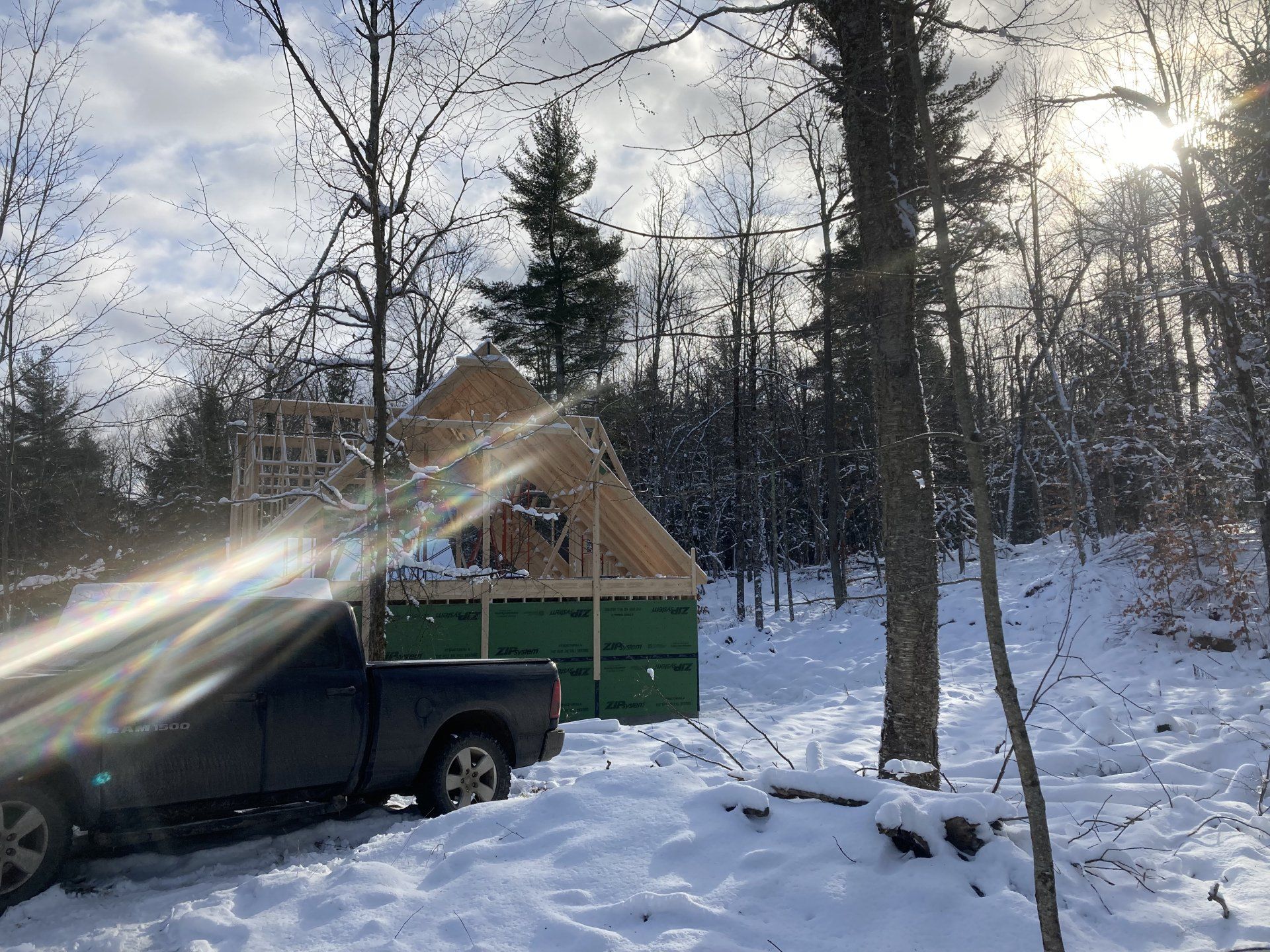 Black pickup truck beside a green cabin in a snowy forest, with sunlight through bare trees.
