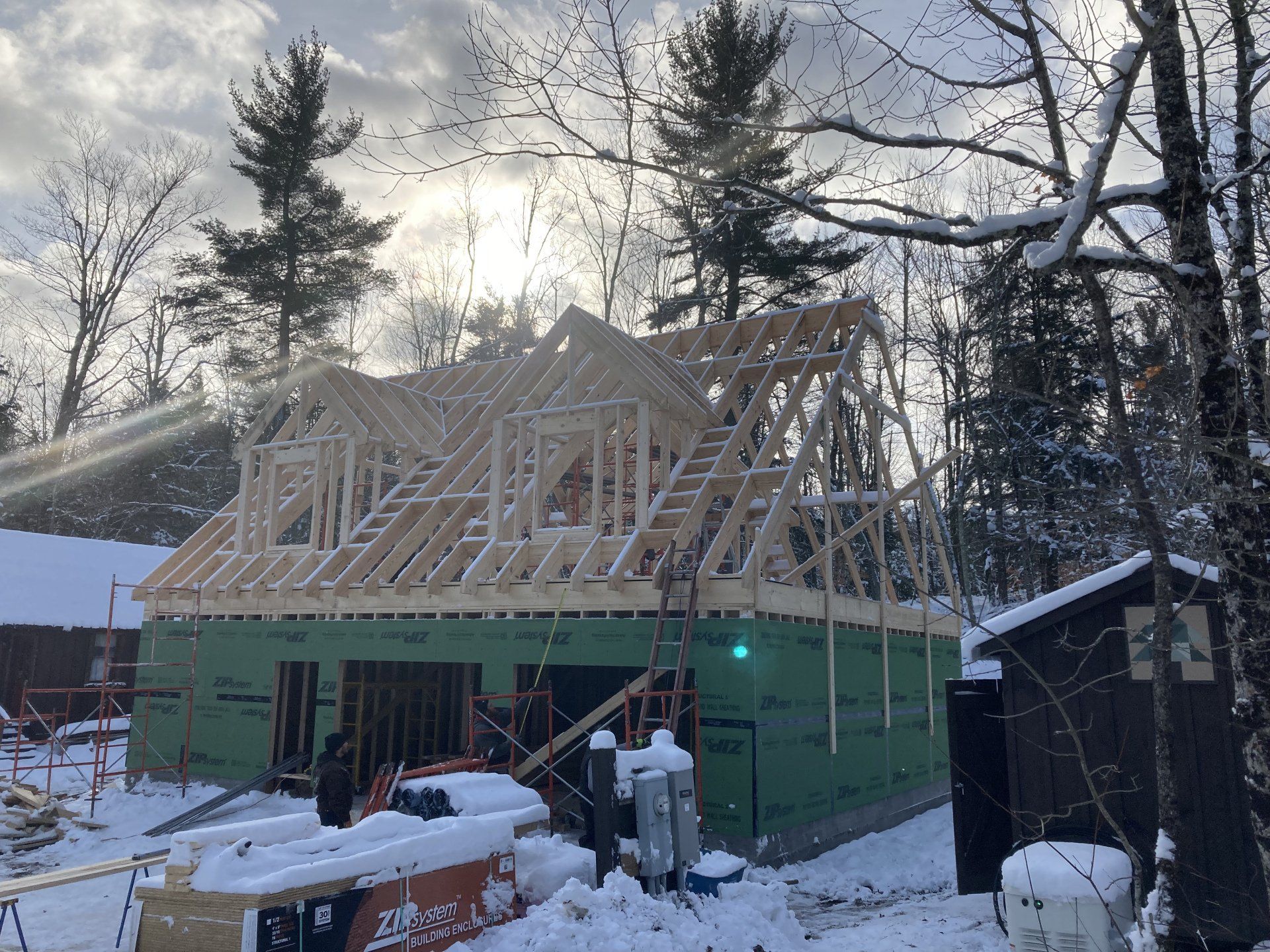 Snowy house construction with workers framing a roof at dusk