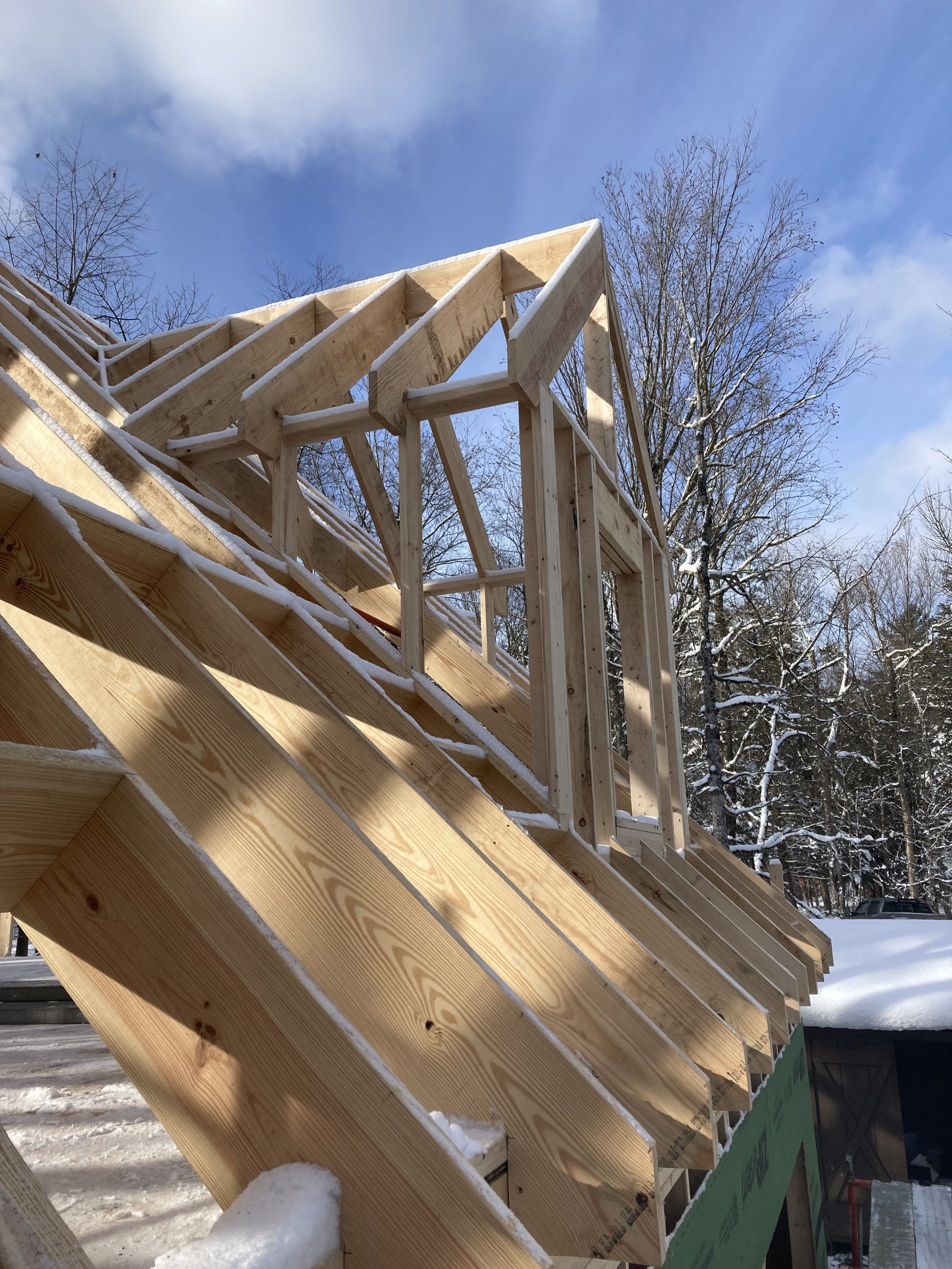 Partially built wooden roof trusses against a blue sky and snowy trees