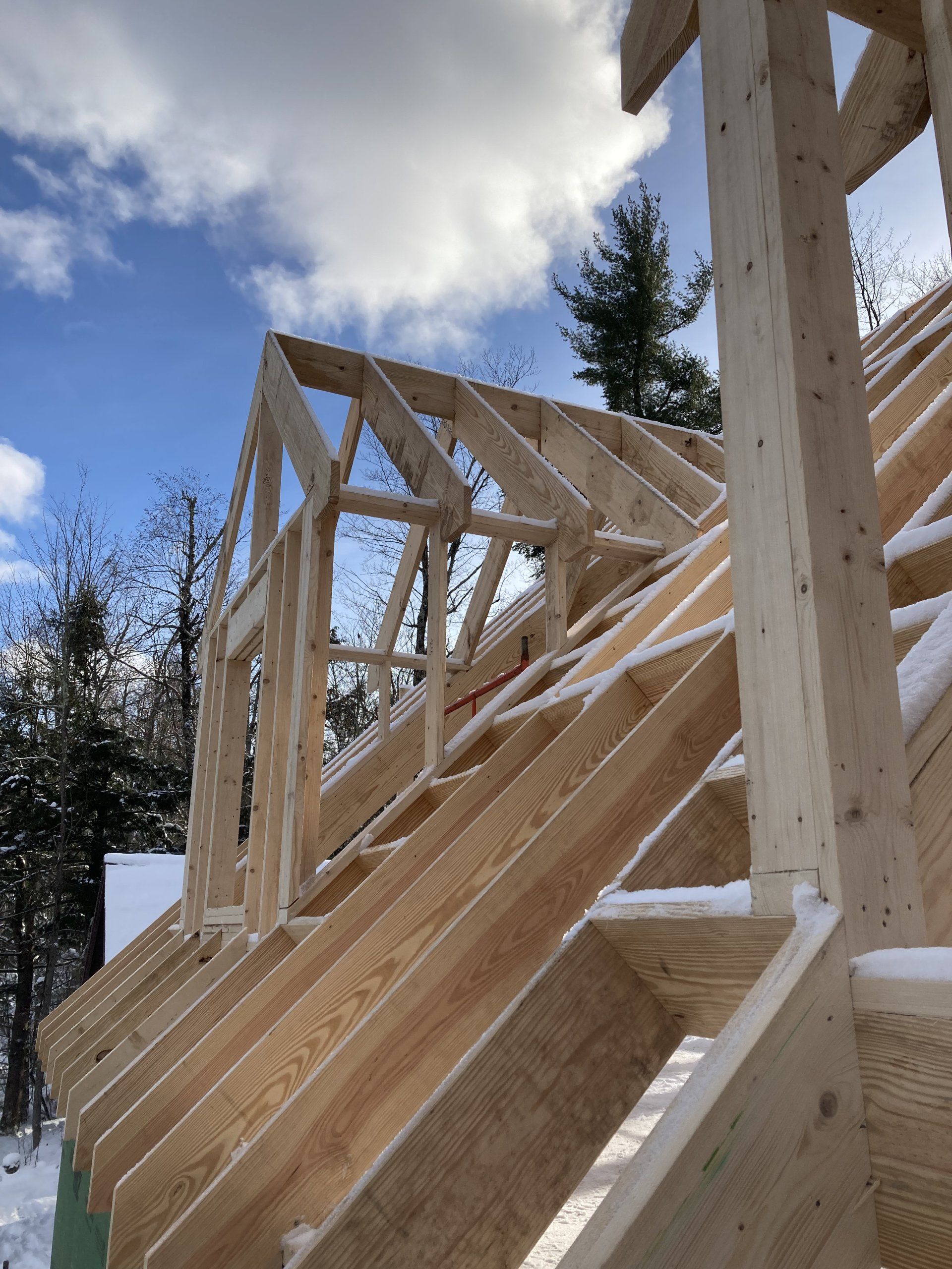 Wooden house framing under construction against a blue sky with clouds