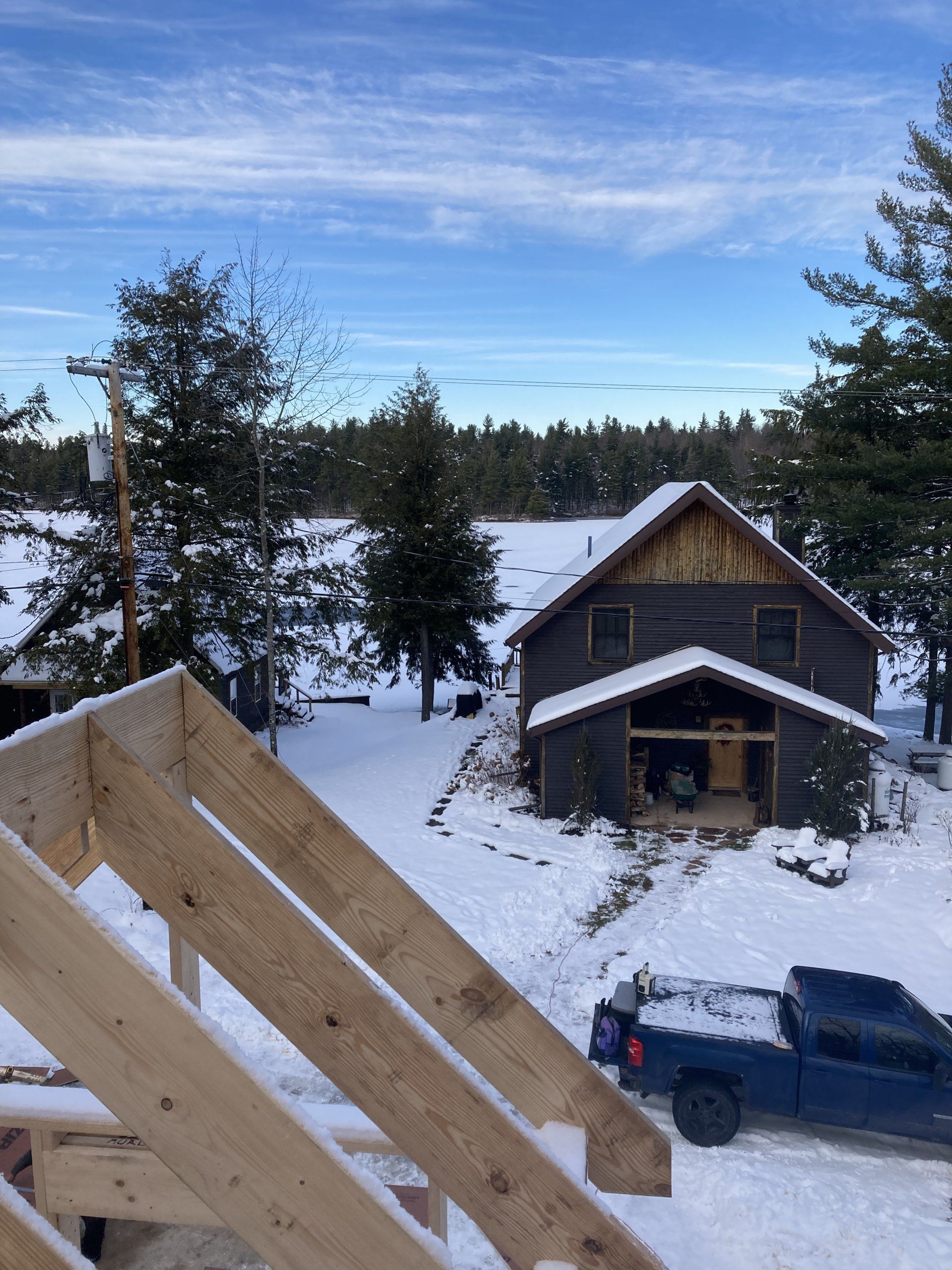Snowy cabin and blue truck seen from a porch under a clear sky