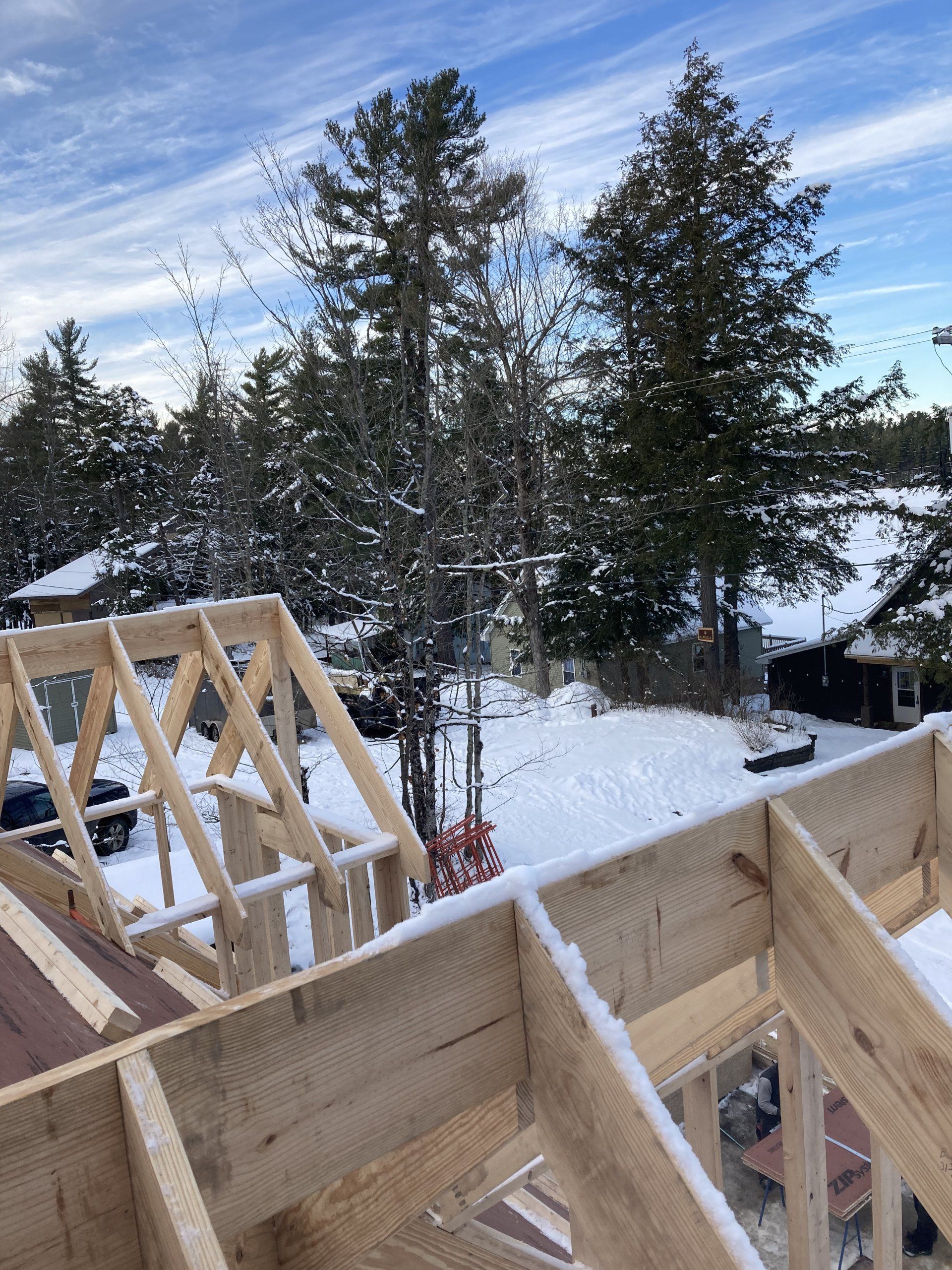 Snowy wooded construction site with wooden roof framing under a blue sky