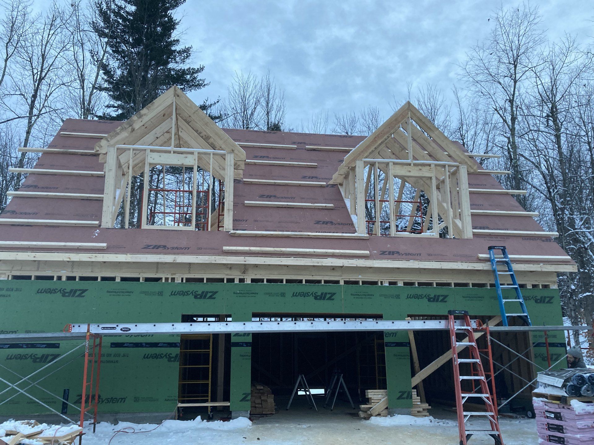 House under construction with roof framing, green sheathing, and ladders on the front porch