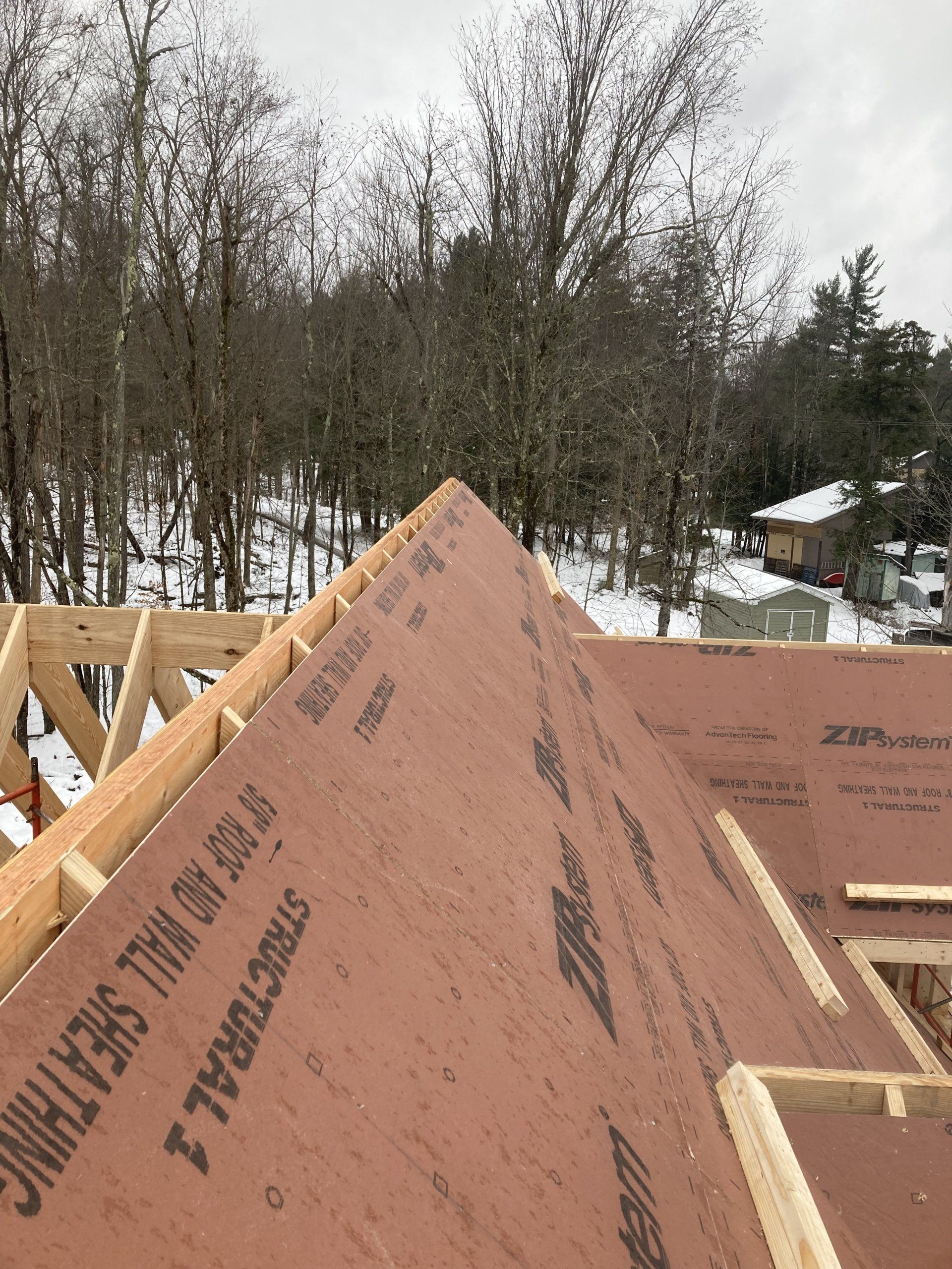 Roof under construction with brown sheathing panels, framed wood, and snowy trees in the background