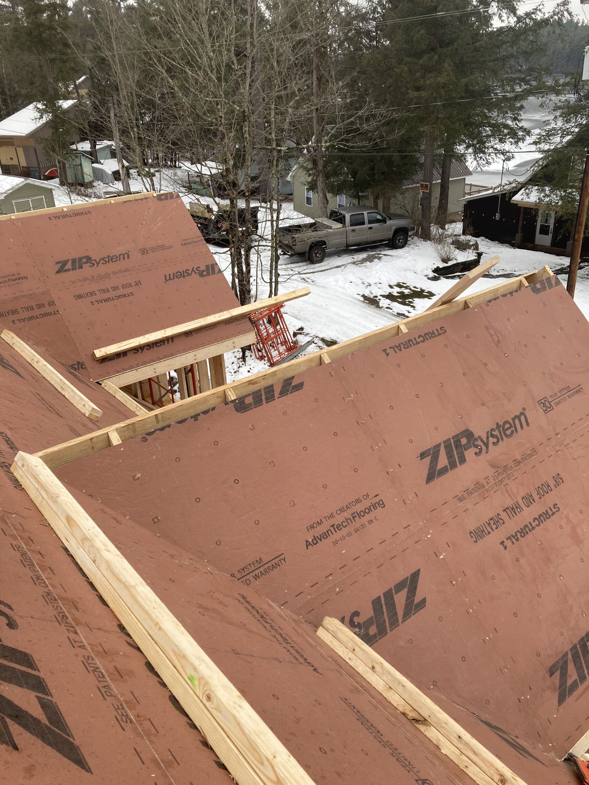 Roofer’s view of plywood roof sheathing and snow-covered neighborhood below