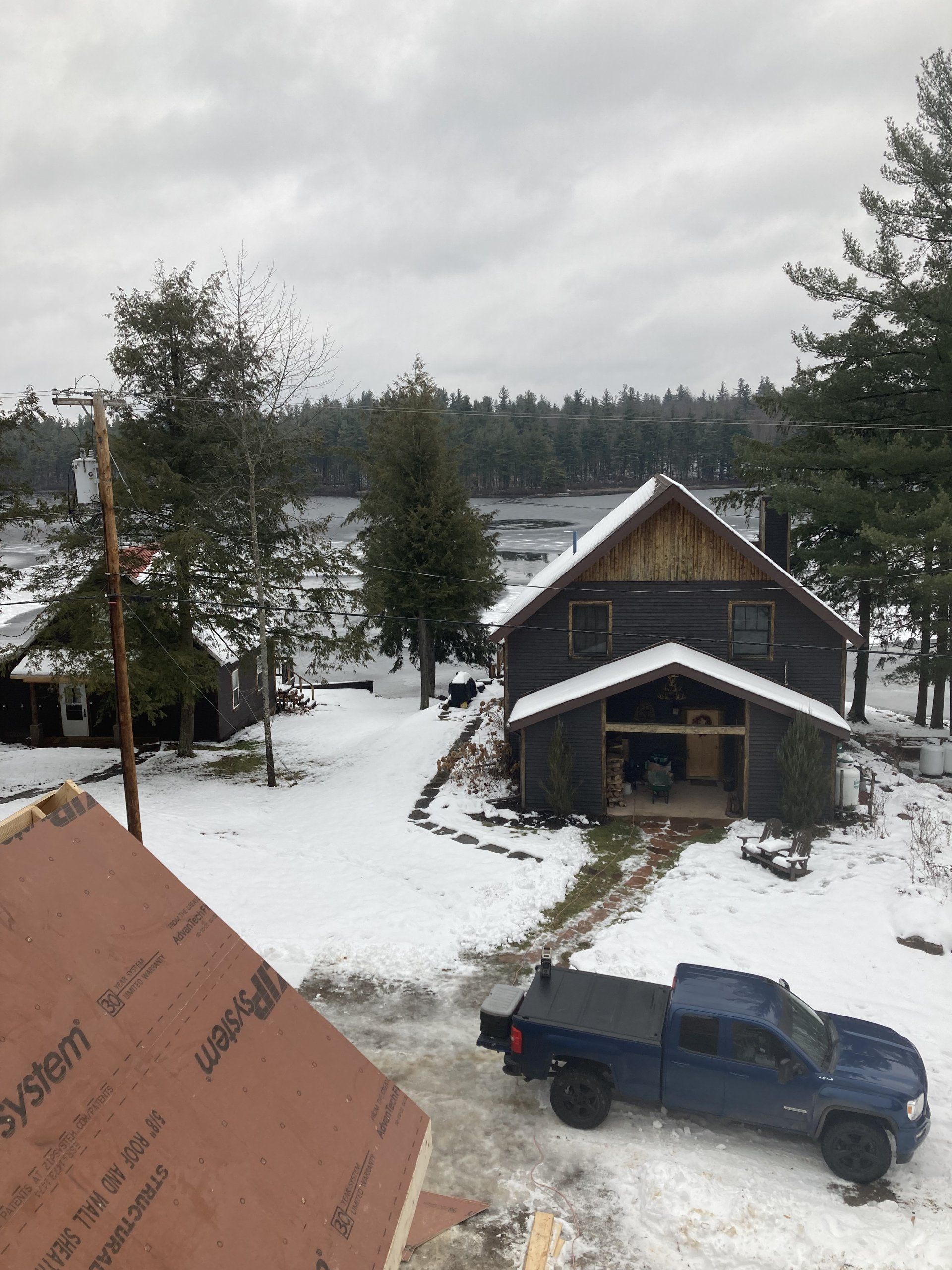 Snowy driveway with a blue pickup truck beside a cabin under cloudy skies