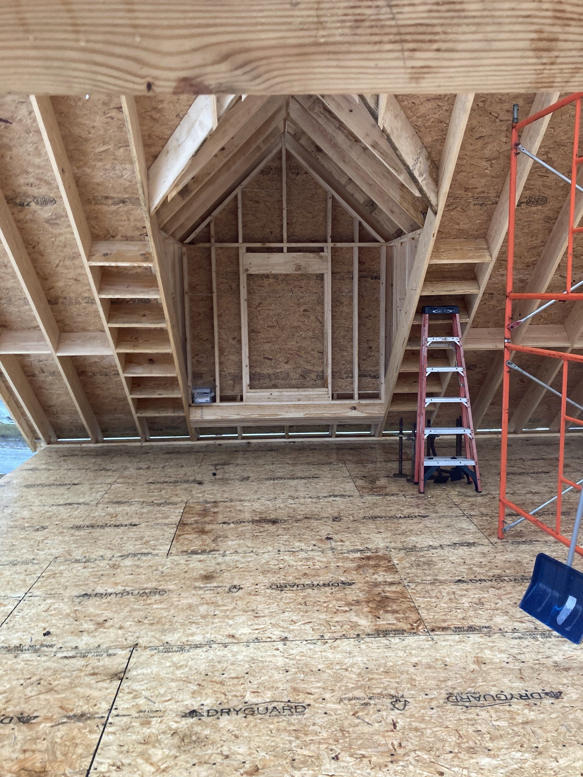 Unfinished attic interior with exposed wooden framing, plywood floor, ladder, and scaffolding.