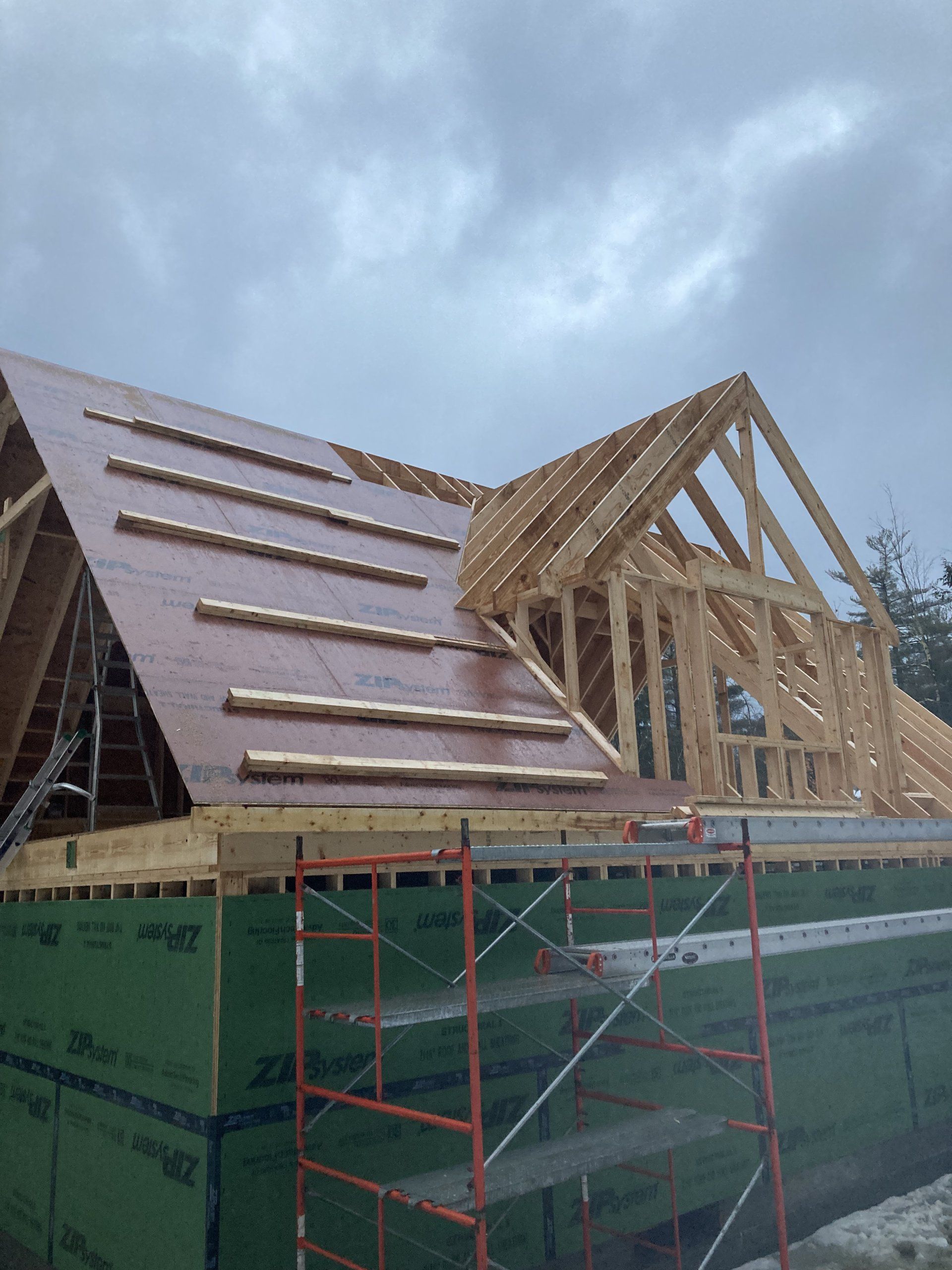 Partially built roof on a house with wooden trusses and green scaffolding under a cloudy sky