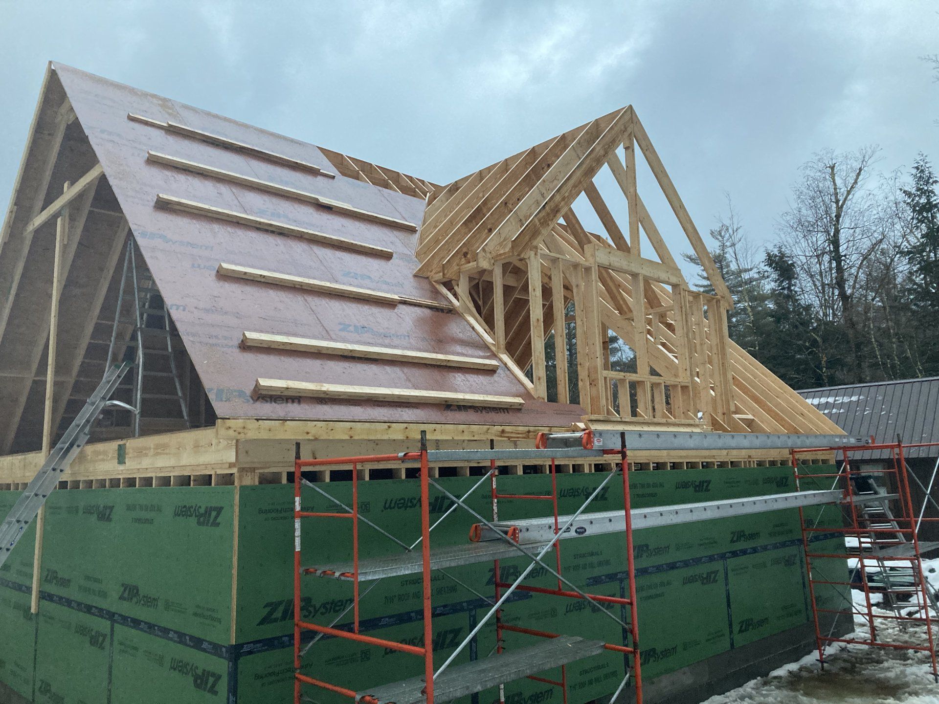 Partially built house with wooden roof framing and green wrapped walls under a cloudy sky