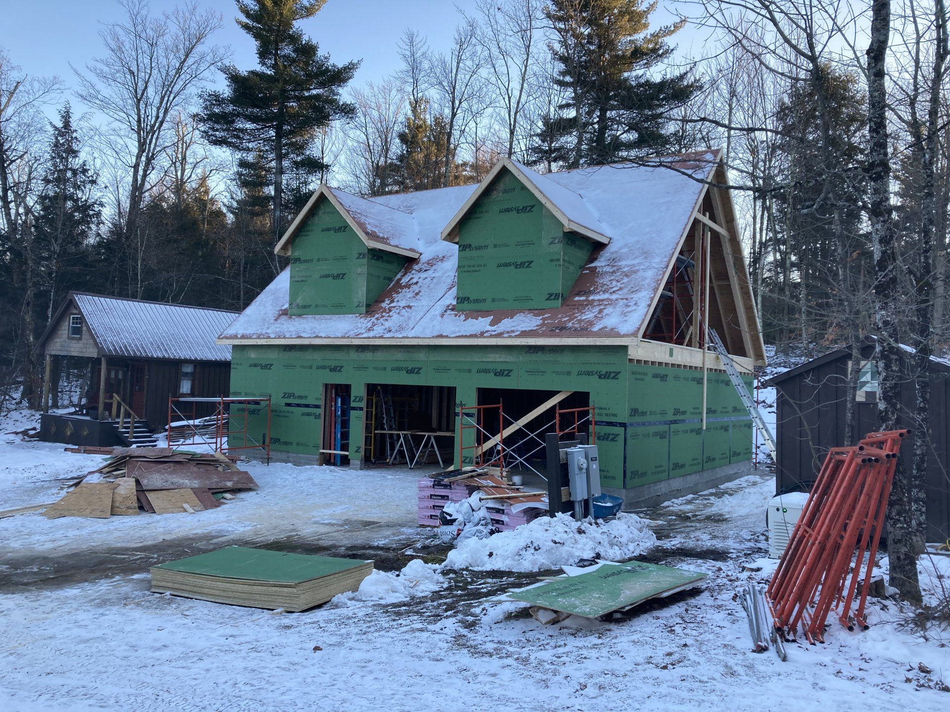 Partially built green house under construction in a snowy yard, with materials and scaffolding nearby