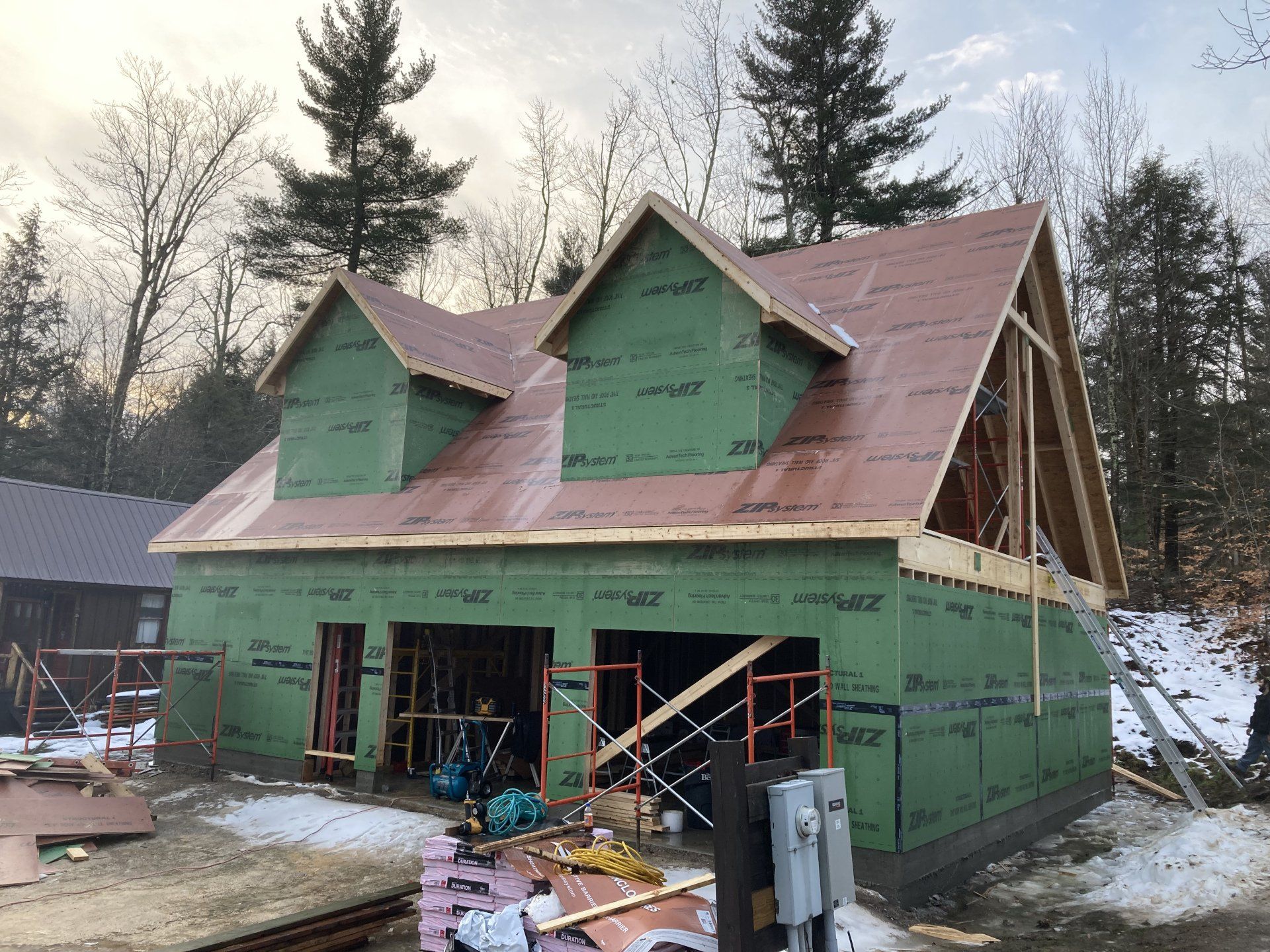 Partially built green house with red roof, scaffolding, and workers at a snowy construction site