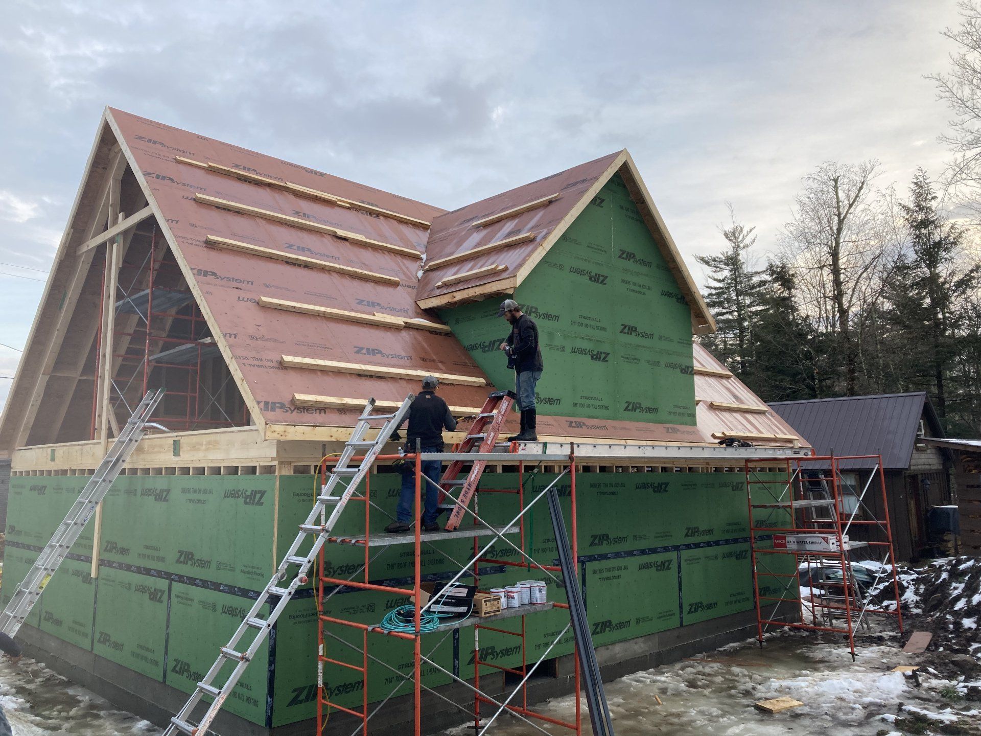 Workers on scaffolding installing a roof on a house wrapped in green sheathing
