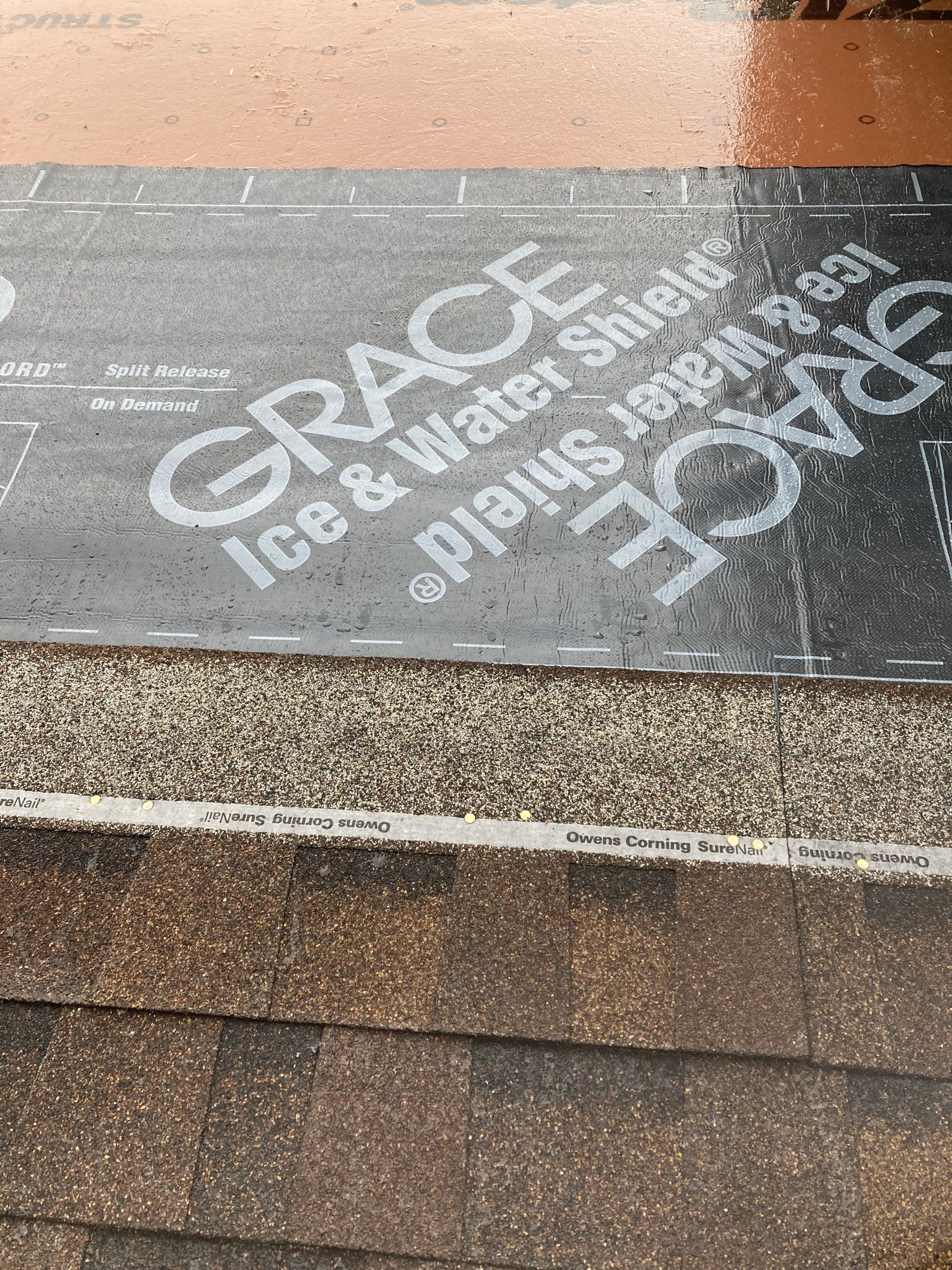 Graffiti on sidewalk reading “GRACE Ice & Water Shield” in white on dark pavement near a curb