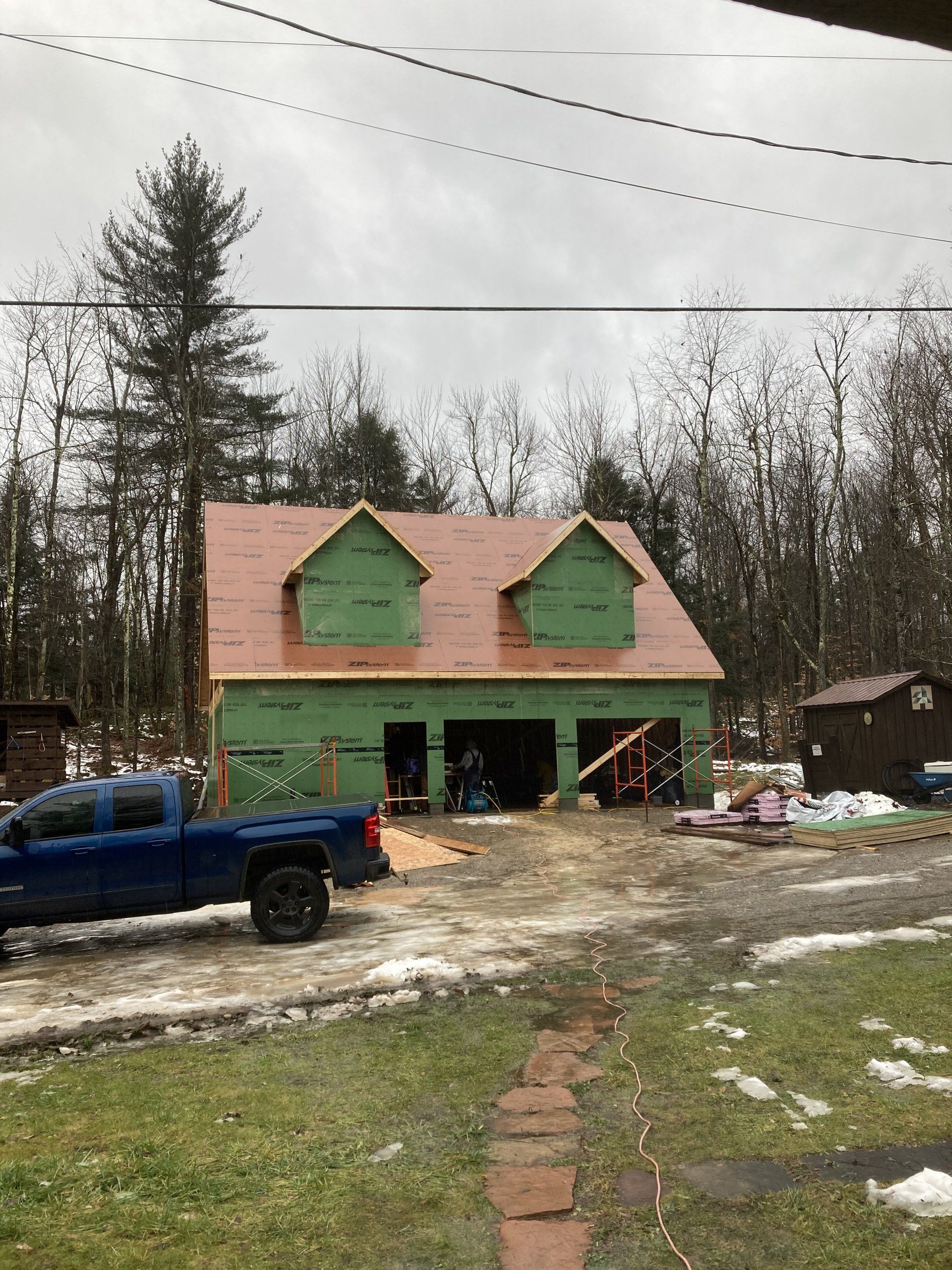Blue pickup truck parked outside a small green-roofed house under construction on a muddy lot