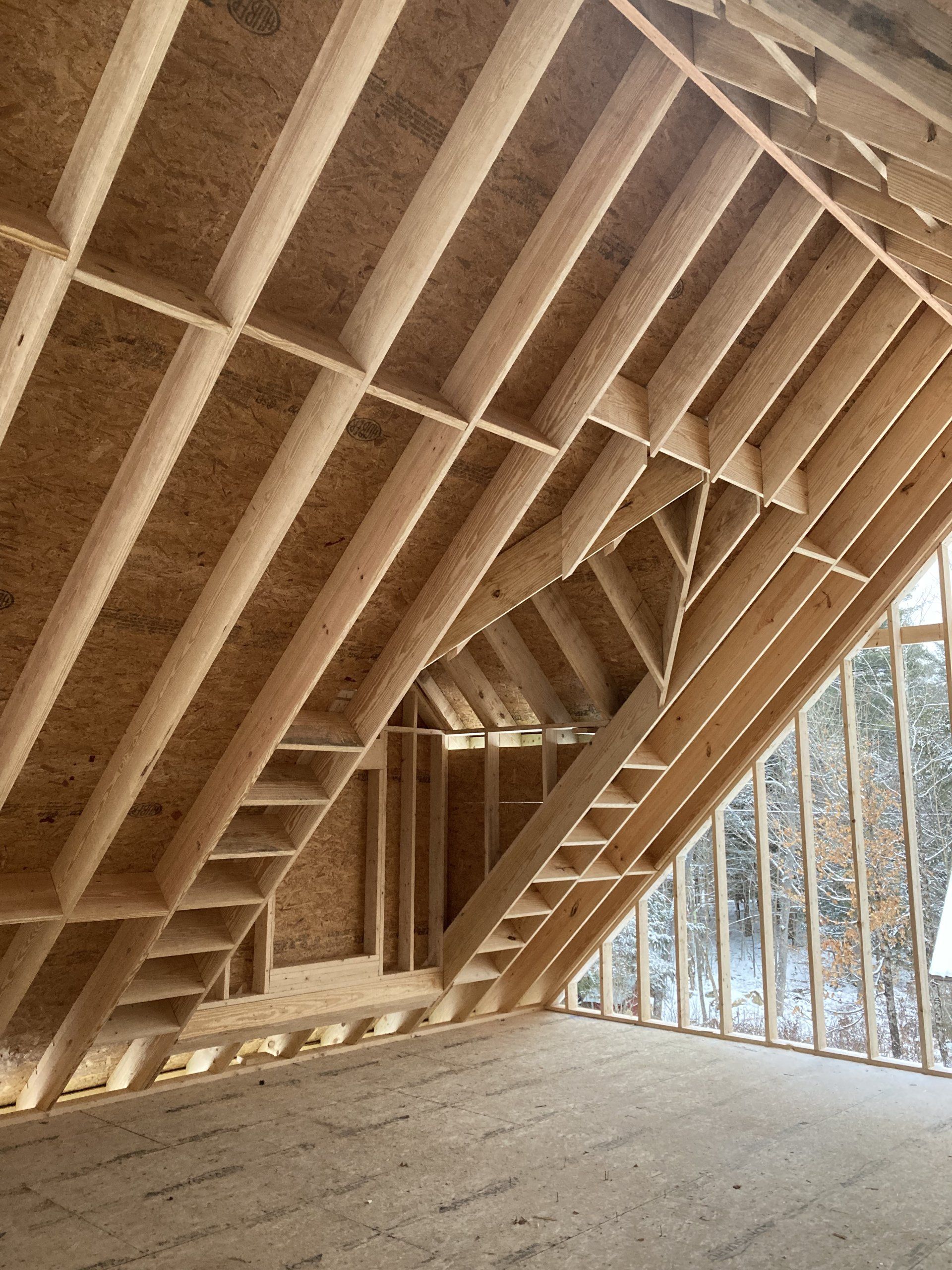 Unfinished wooden attic framing with exposed rafters and insulation, lit by daylight through a wall opening