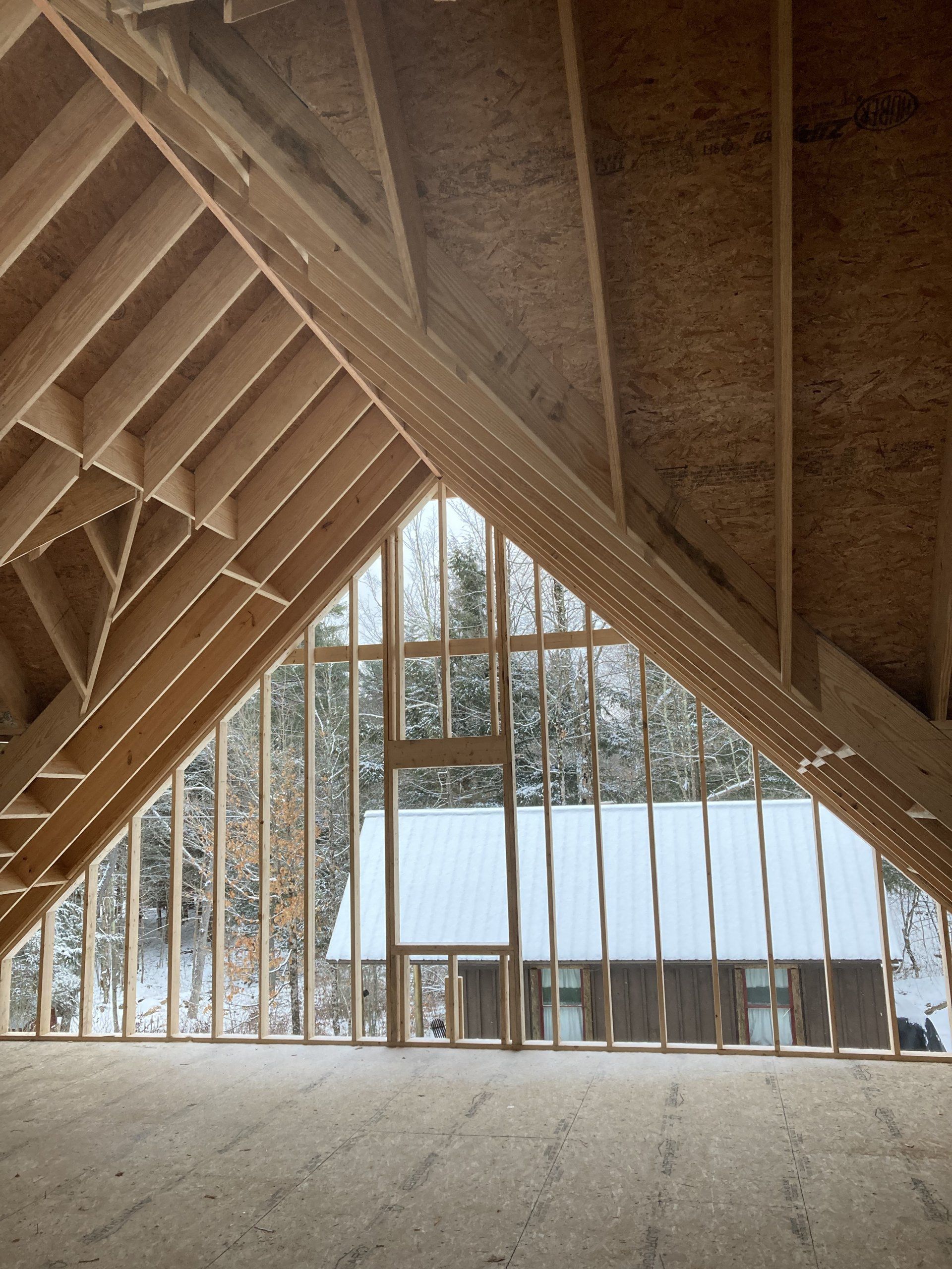Wood-framed A-frame interior with large windows overlooking a snowy landscape.