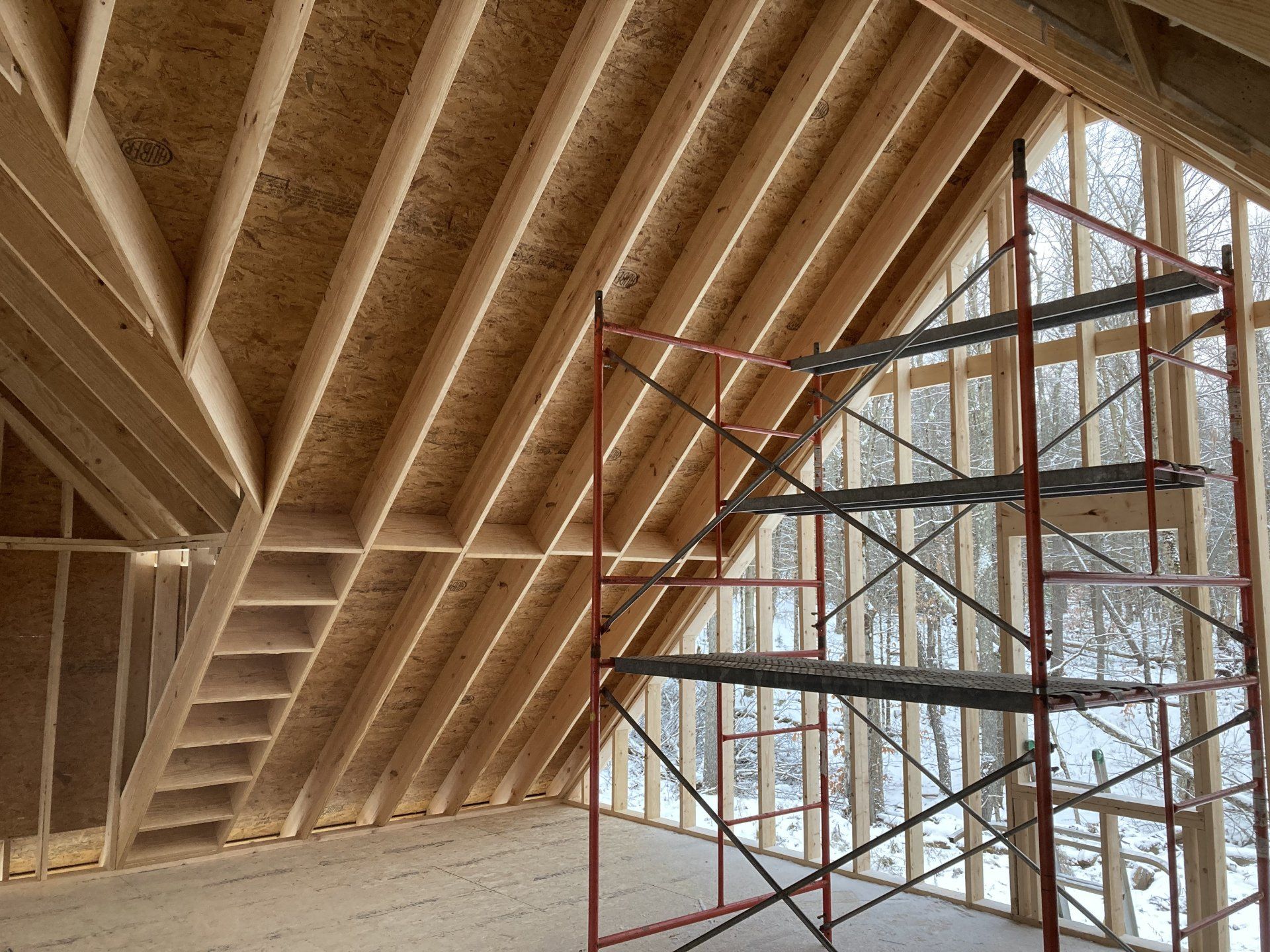 Interior of a wooden house under construction with exposed roof framing and scaffolding by large windows