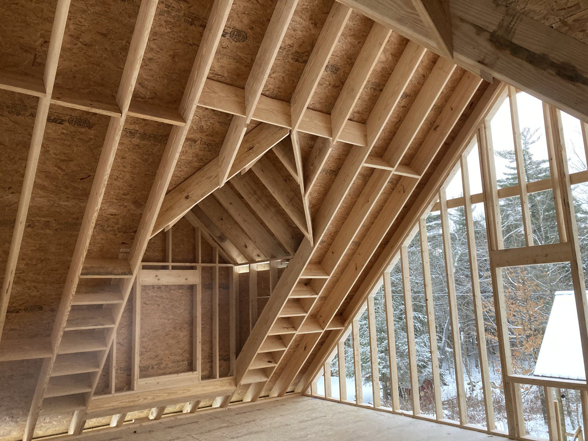 Wood-framed attic interior with exposed beams and a large slanted wall of windows.