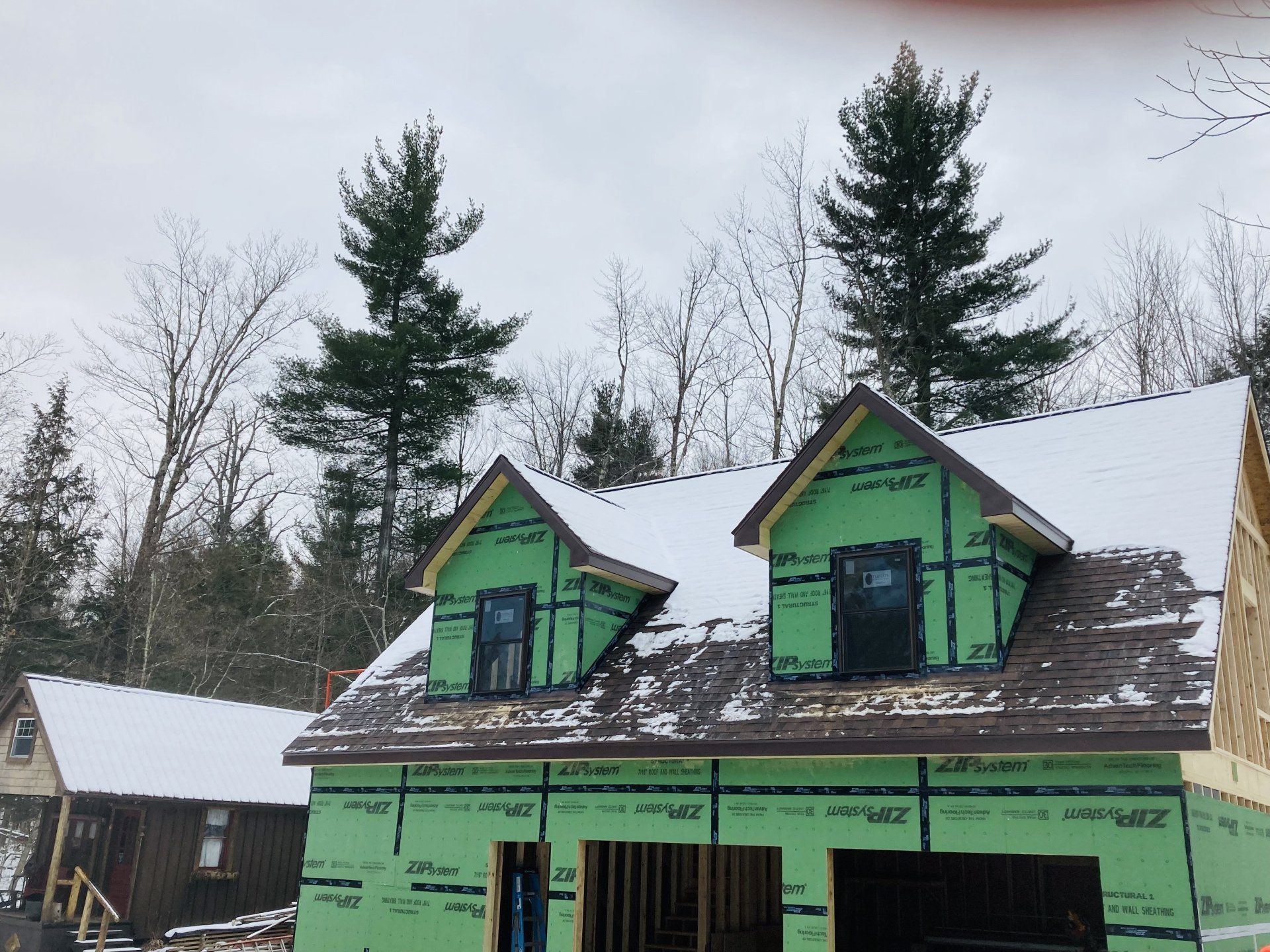 Green house under construction with snow on the roof and trees in the background