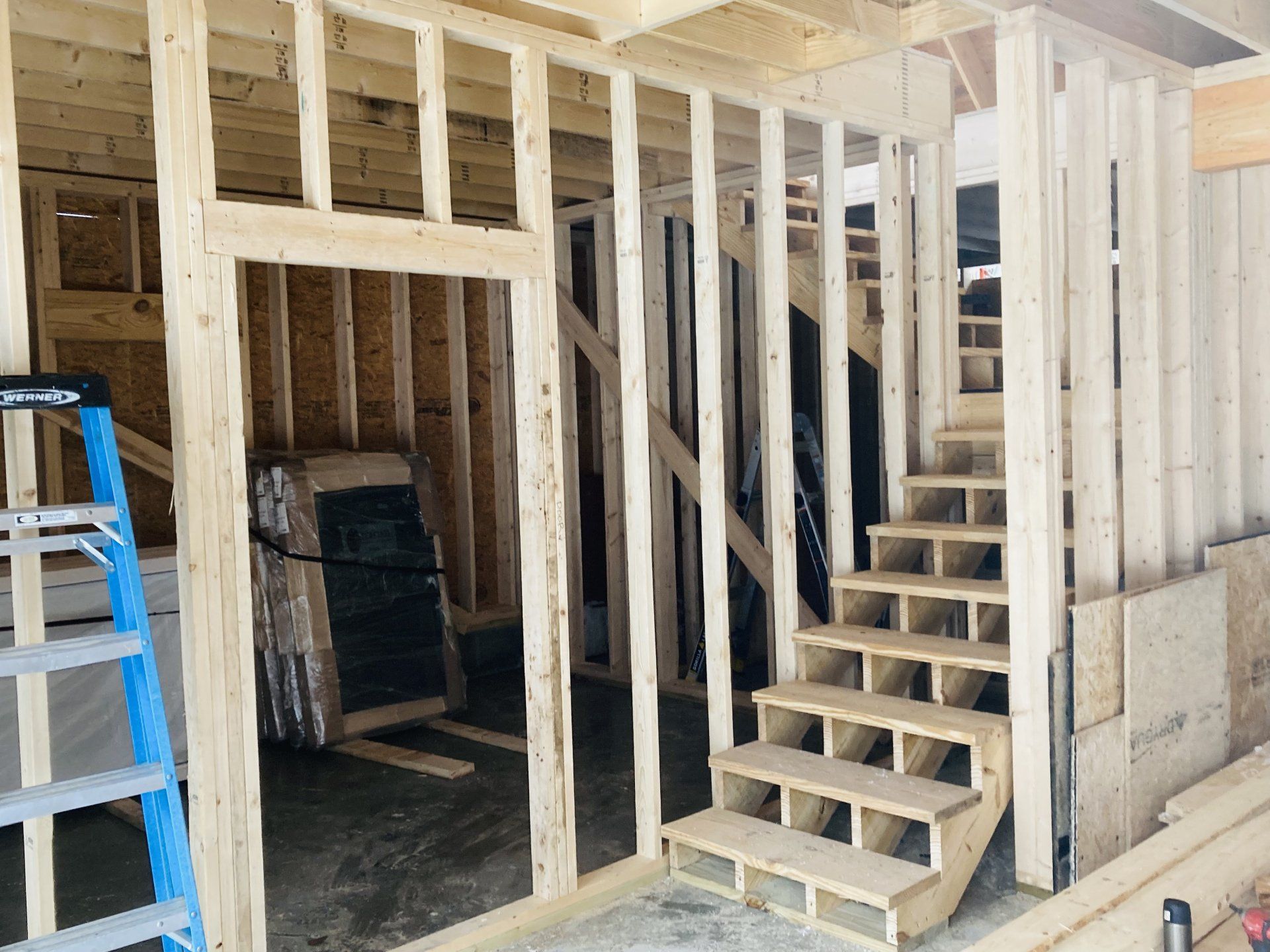 Unfinished interior with exposed framing, a staircase, and a blue ladder in a construction area