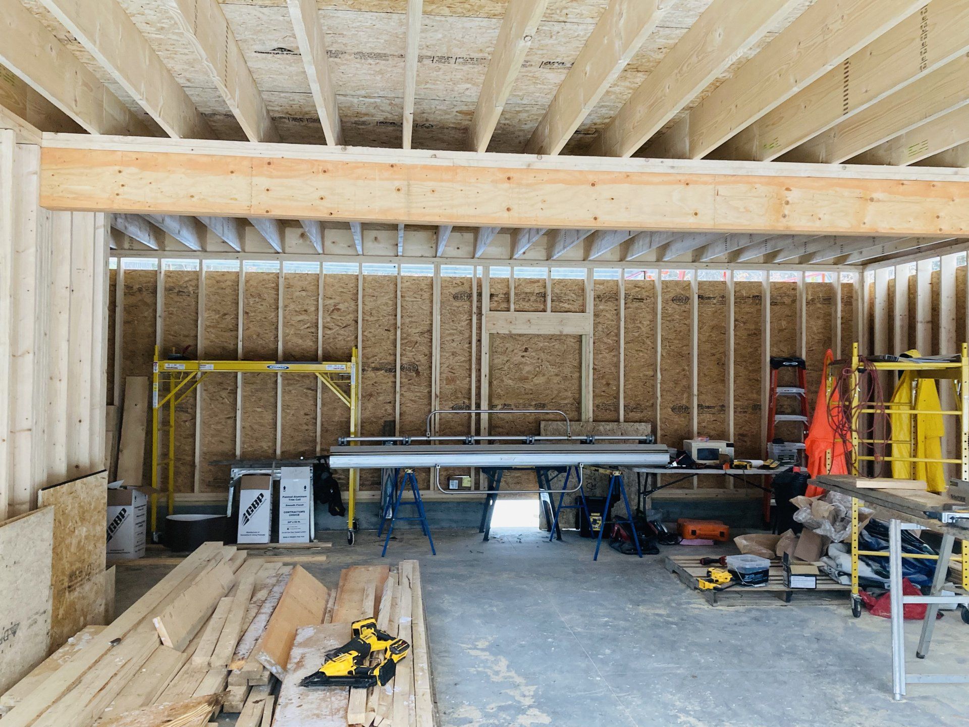 Unfinished garage with exposed framing, stacks of lumber, tools, and workbenches inside.