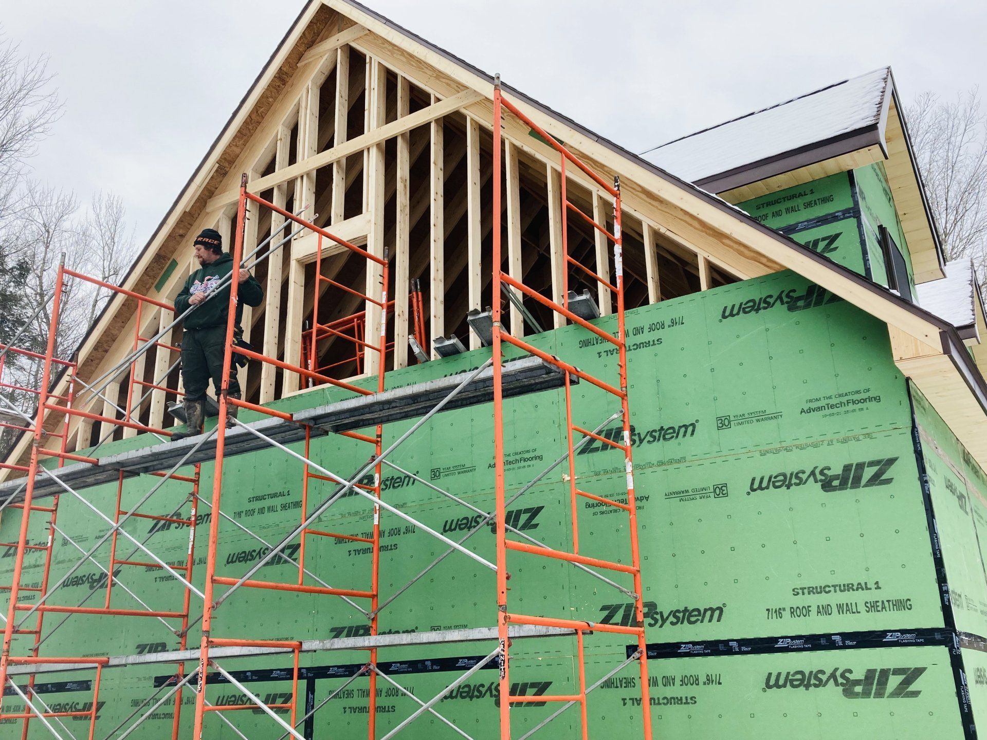 House under construction with green sheathing and orange scaffolding around a peaked roof.