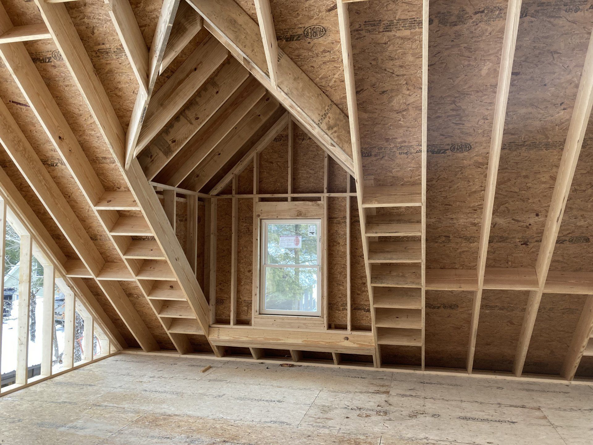 Unfinished attic with exposed wooden framing, sloped roof trusses, and a small window letting in daylight