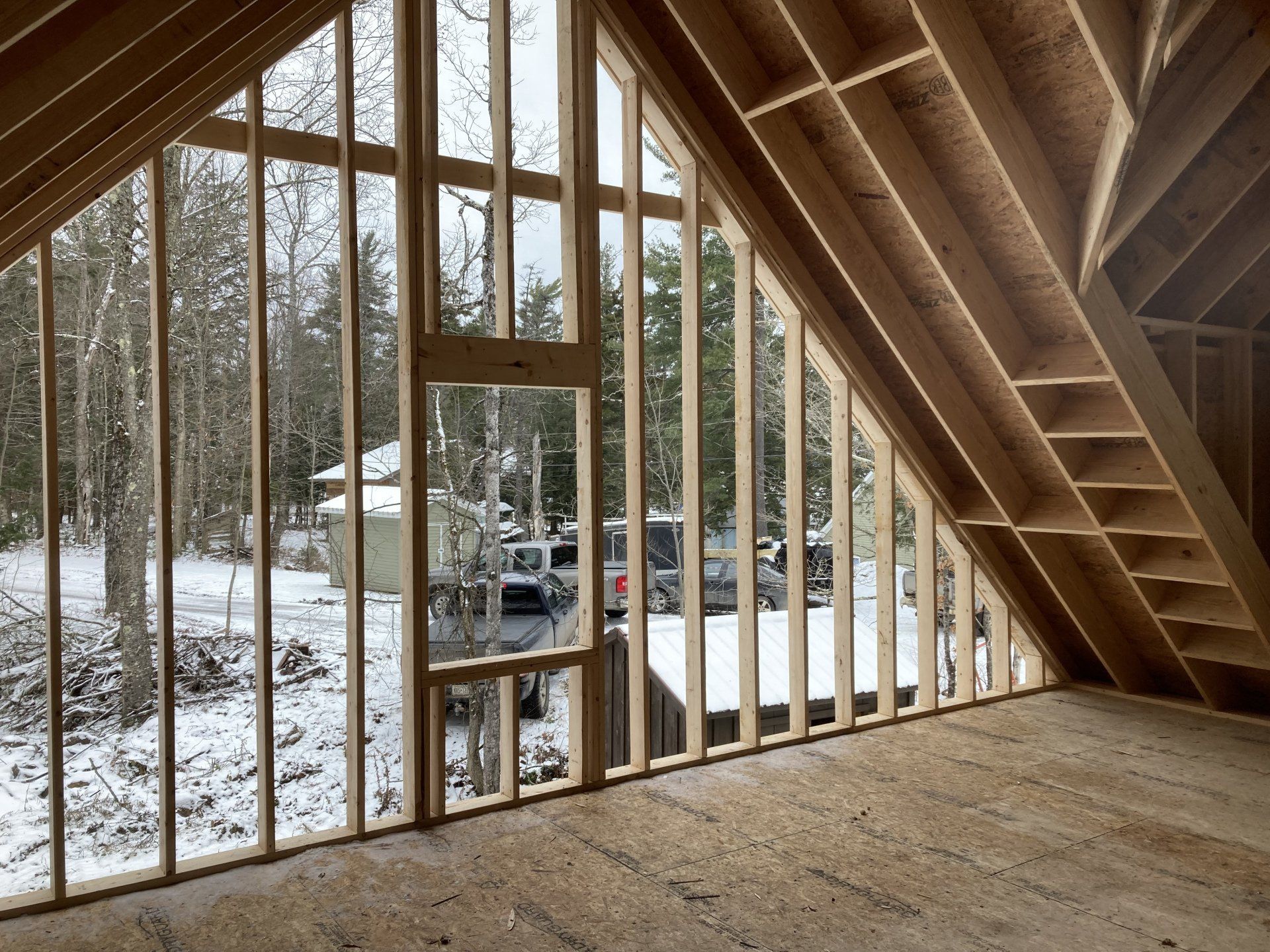 Unfinished attic with exposed wood framing, snowy view outside, and a parked vehicle visible through the window.