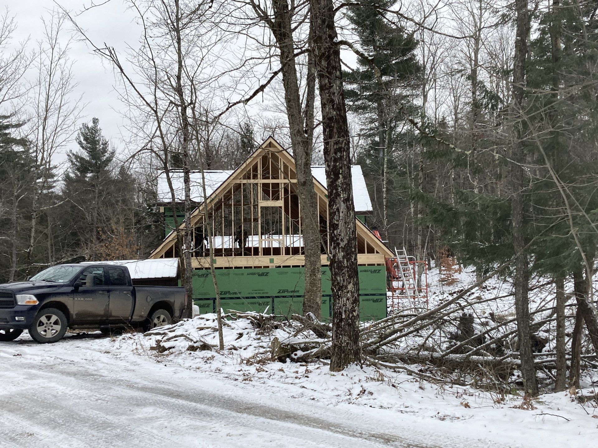 Partially built cabin with green tarp in snowy woods, with a pickup truck parked beside it